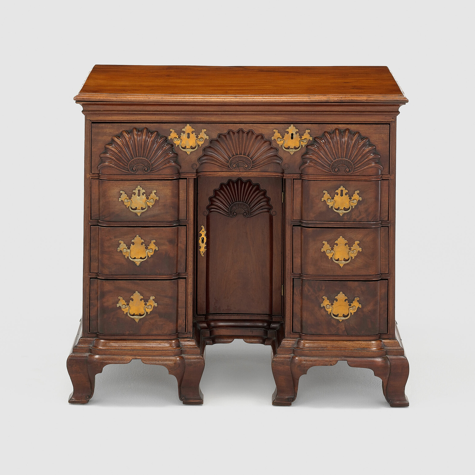 Small wooden bureau with carved half-circle designs, gilded handles.