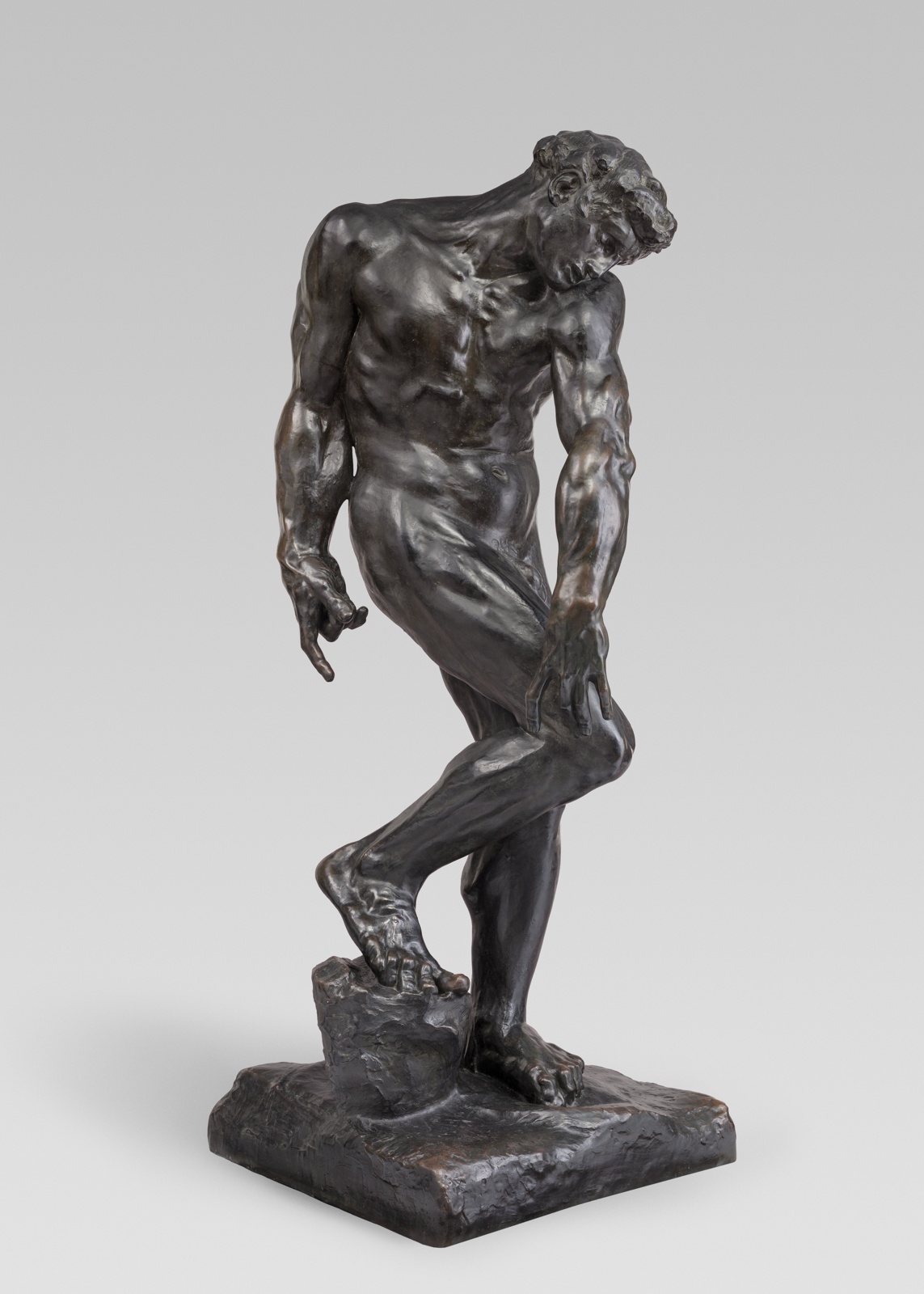 Dark colored sculpture of muscular man standing in a contorted pose.