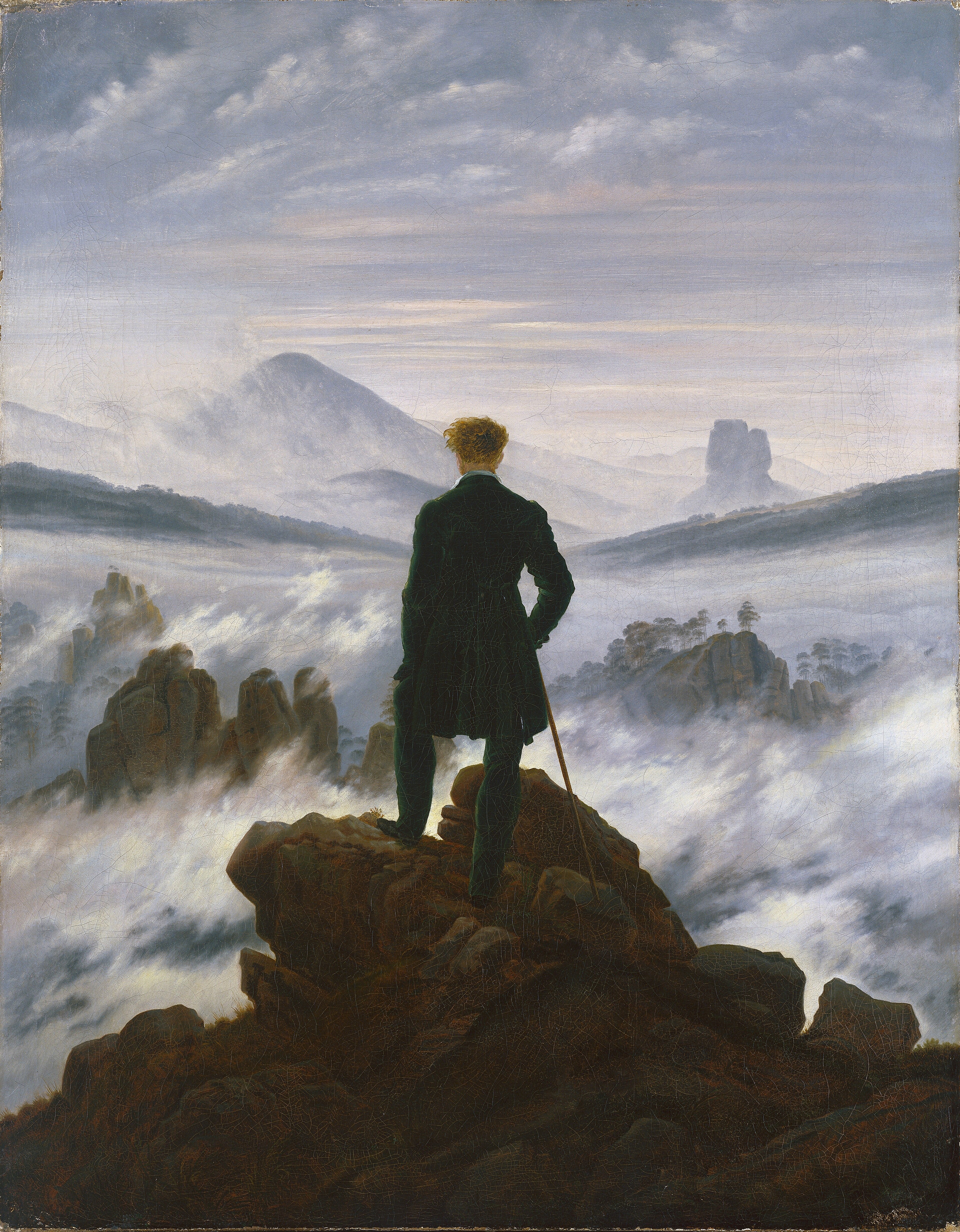 Friedrich: a solitary man seen from behind on a rocky peak above fog and distant mountains.