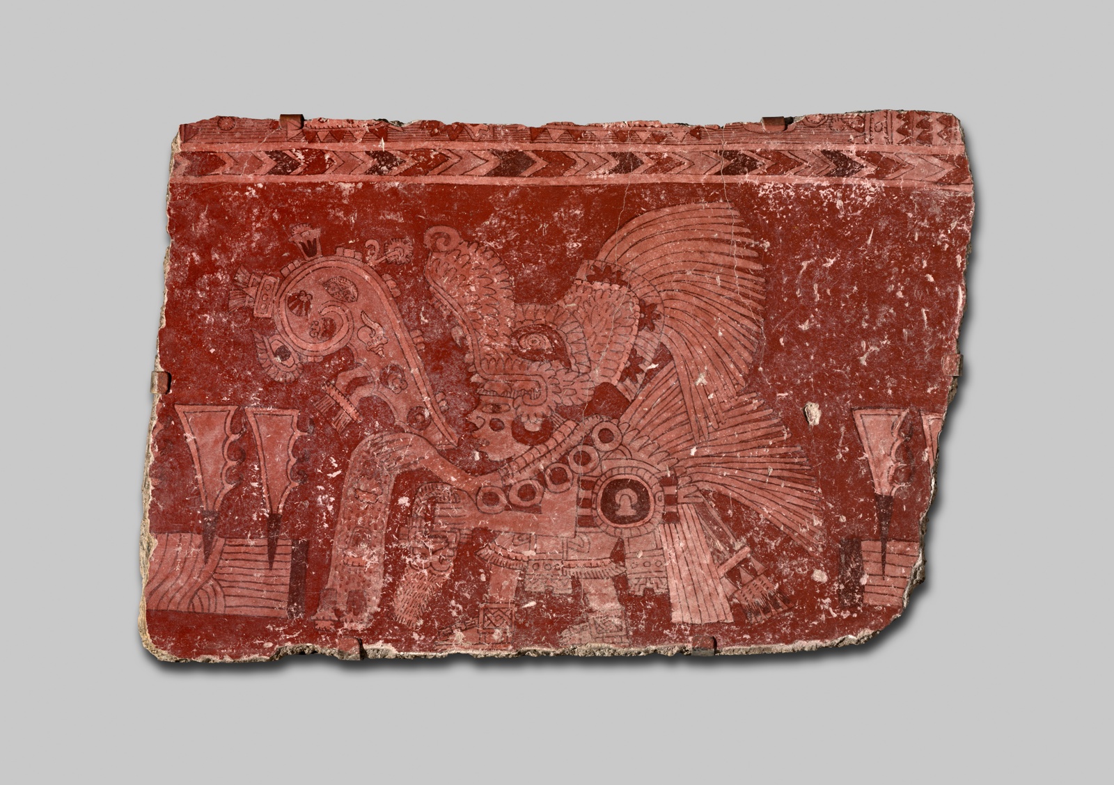 Fragment of a mural from the city of Teotihuacan mural painted in red and white tones that depicts a ritual figure with speach scroll and scatting sacred bjects.