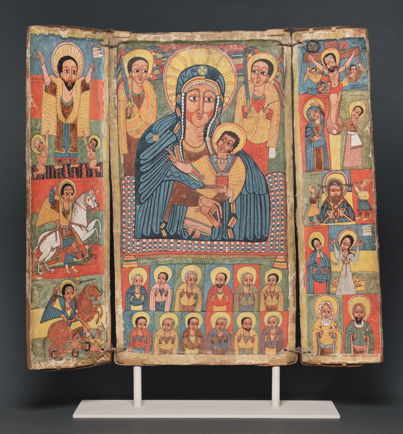 A three-part panel featuring a variety of scenes, vertically stacked and richly painted. The central panel features the Virgin Mary and and Child flanked by archangels Gabriel and Michael, twelve disciples below them in grid formation.