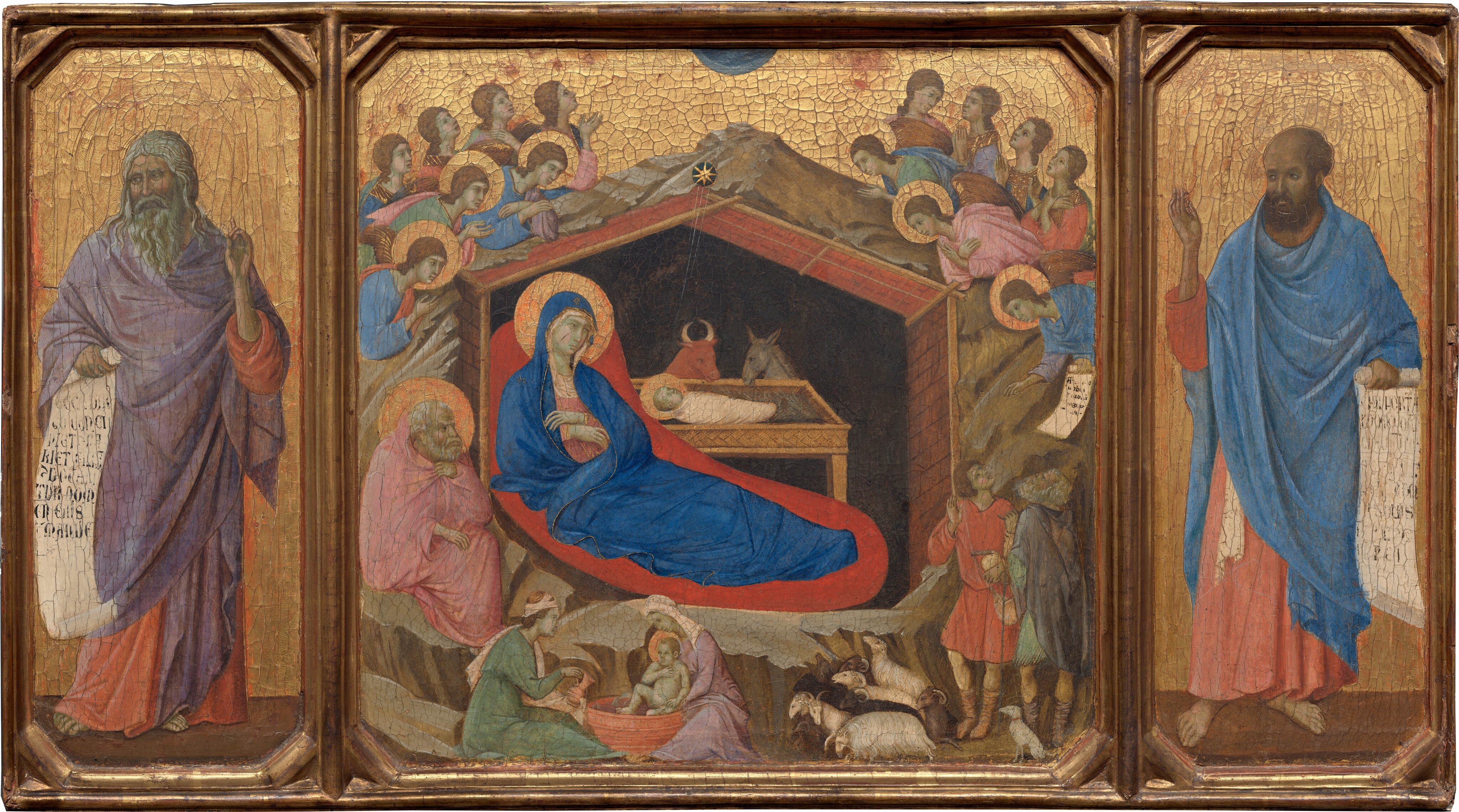 This horizontal painting is made up of three parts: in the center square panel, a woman reclines under a wooden shelter set into a rocky cave, which is surrounded by angels, and narrower wings to either side are each occupied by a standing man. All the people have pale skin, which is tinged with faint green. The three panels are joined with a gold frame, and the gold background behind the central scene and the men in the side panels are covered with a noticeable network of cracks. In the central panel, a cobalt-blue robe nearly envelopes the reclining woman’s body; this is Mary. It covers her head and falls open where she crosses her wrists over her chest to show a pink garment underneath. A flat gold halo encircles her head ,and her body is surrounded by a field of crimson red, almost like an aura. She rests under a wooden structure with a pitched roof, which is surrounded by craggy, barren rock. A swaddled infant lies in a rectangular, tray-like manger. The infant’s head is also surrounded by a gold halo. Fine gold rays emanate down into the structure from a star just above the peak of the roof. A bull and a donkey look down at the baby from the far side of the manger. The interior of the structure behind them is black. In a smaller scale, two women wash a haloed infant in a tub in front of the rocky cave near the lower left corner of this panel. A man with a white beard and hair sits to our left of Mary, holding a pink cloak at his throat and looking toward the infant. Above and around the rocks, seven winged and haloed angels cluster on each side. One angel to the right presents a scroll with black writing to two men accompanied by a dog and several sheep in the lower right. The man in the panel to the left, Isaiah, has a gray beard and long, wavy hair, and he wears a lilac-purple cloak draped over a coral-orange robe. In his right hand, on our left, he holds an unfurled scroll with large black lettering. His other hand is raised with one finger pointing upward. He looks to our left, away from the central scene. On the right, Ezekiel, echoes Isaiah's pose. Ezekiel holds an open scroll with his left hand, on our right, and his other hand is raised. He also wears a coral-colored robe, but his is overlaid with a blue cloak. His receding hair is short and brown, as is his beard. Like Isaiah, he takes up most of the height of the panel and gazes to our left, toward the central panel.