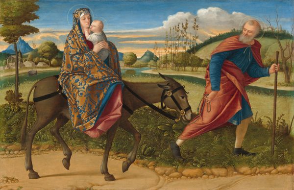 Close to us, a bearded, balding man leads a donkey carrying a woman and child to our right against a hilly landscape in this horizontal painting. All three people have pale, peachy skin and halos. The man has a gray beard and hair, and wears a royal-blue tunic under a ruby-red robe. He leans on a walking stick and looks back at the donkey. The woman riding the donkey wears a blue and gold brocade-like cloak covering her head and body. She has a straight nose, small pink lips, and she looks toward the infant she holds close to her body. The baby wears a white garment and reaches for the woman’s face with one hand as he turns to look over his shoulder toward us. The path they walk on is lined with grass and detailed plants. A river runs parallel to the path a short distance away. The horizon line comes about two-thirds of the way up the painting is lined with green trees, blue mountains, and a few buildings to our left. Wispy white clouds sweep across an azure-blue sky streaked with peach near the horizon.