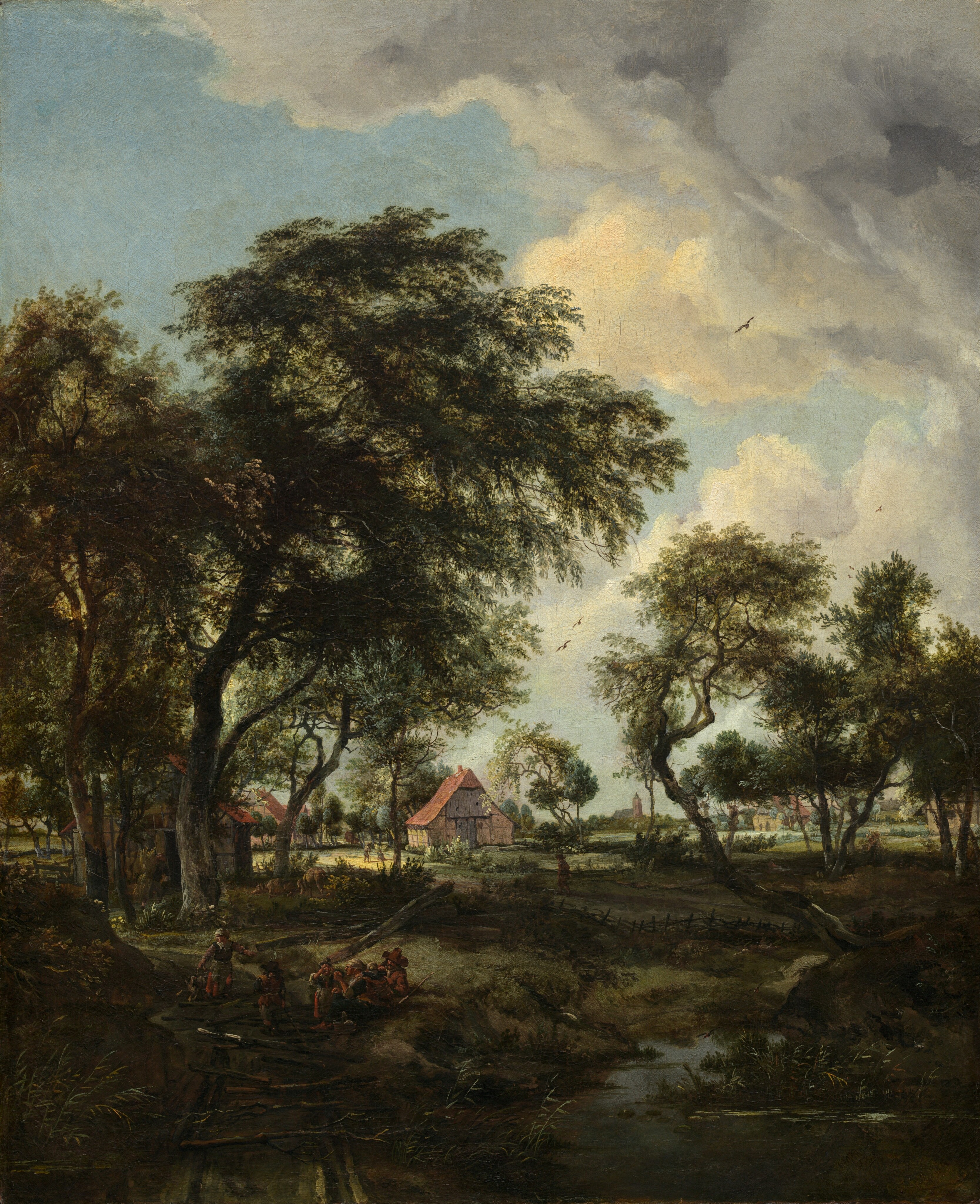 We look across a stream and through a loose screen of shadowy trees at a sunlit farm under a powder-blue sky with towering, puffy clouds in this vertical landscape painting. The ground and stream closest to us are painted in tones of olive green, sepia and earth brown, black, and slate gray. Nearly lost in shadow, a group of six people gathers at the water’s edge in the lower left. Small in scale within the composition, they wear brick-red, gray, or caramel-brown garments. Beyond them, a low picket fence winds through and between a loose band of shadowy trees, which are painted with gnarled, dark gray trunks and camel-brown, sage, and pine-green leaves. The trees to our left are closer and taller, while those to our right are a little farther away. The sun pours from the upper left into the field beyond. The farm buildings there have tan walls and sloping, peach-colored roofs. A few animals and people, smaller than the group in front, stand among the buildings, and more cottages can be glimpsed through a stand of trees on our right. The horizon line comes about a third of the way up the composition, and a church and steeple are silhouetted against the sky in the deep distance. A few birds fly in front of gray and white clouds that rise from the right side and spread across the top of the canvas.