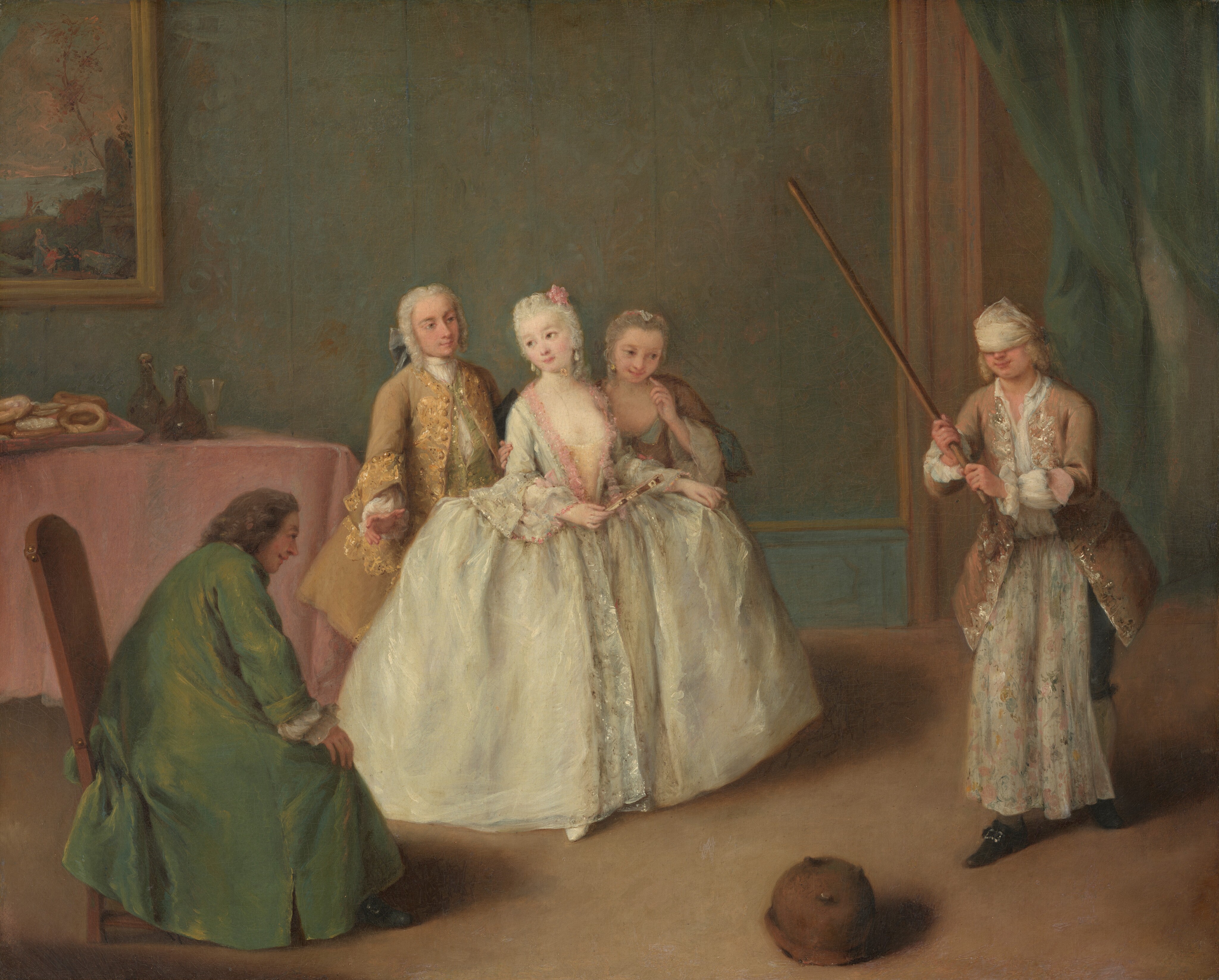 This painting shows five individuals in an indoor setting. Four are standing, while one person with long dark hair is seated on a chair in the bottom left corner, wearing a long dark green robe. In the center of the painting is a group of three people, including a man in a light gold embroidered coat and white breeches with a white wig. In the middle of this trio is a woman in an elaborate ivory gown with pink lace details, holding a fan and wearing a floral pink accessory in her white powdered hair. Another woman stands slightly behind her, dressed in a brown gown with gray styled hair. On the right, a blindfolded man stands and holds a wooden stick, wearing a long brown coat with silver embroidery, a white blindfold, and a white wig. A floral, light-blue cloth has been tucked into the front of his pants, covering blue breeches. All of the people in the painting have pale skin. The floor is light brown, and a small, round, brown object is on the floor in front of the group. The background includes a table with a pink tablecloth, wine bottles, and pastries, below a framed painting on the wall. The wall is a pale, blue-green color, and green drapes hang on the right side of the room next to a brown opening.