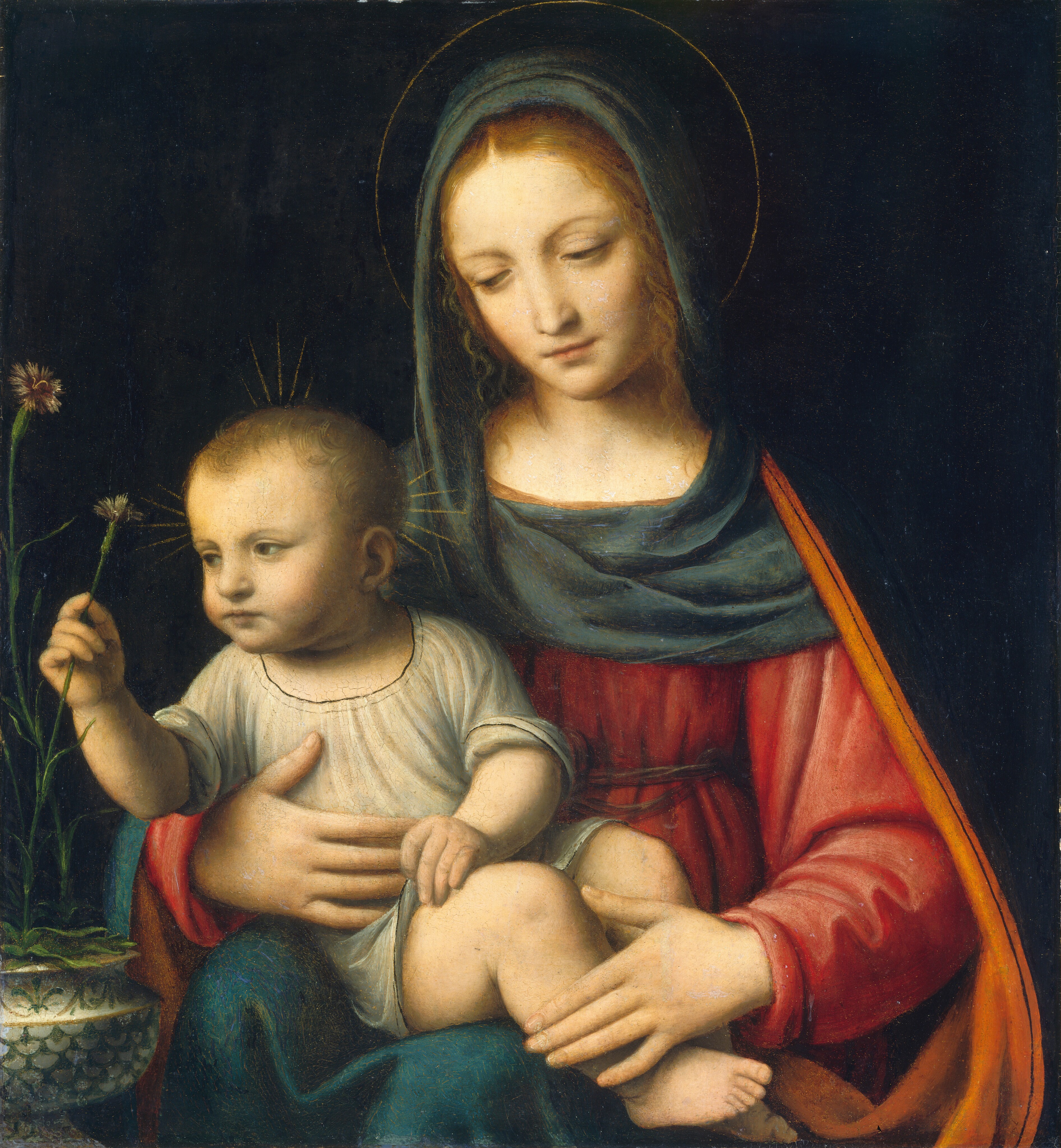 Shown from the lap up, a young woman sits facing us as she cradles a plump baby in her lap in this square painting. They both have pale, peachy skin and blond hair. They are softly lit from the upper left, and the background behind them is inky black. A sea-blue cloth drapes over the woman’s head and across her shoulders. Its top edge is rolled back slightly, revealing tendrils of long, wavy hair framing her face. A thin gold line creates a delicate halo around head. Her scarlet-red gown is gathered and belted high above the waist. A cobalt-blue mantle lined with pumpkin orange drapes down over her shoulders, the arm of her chair, and her lap. She tilts her head slightly to our left, and lowers her eyes to gaze at or toward the child. She holds his torso with her right hand, to our left, and rests her other hand across his ankles. The child wears a dove-gray tunic with rolled up sleeves. His short hair lies in flat swirls, and his chubby cheeks are tinged with pale pink. Clusters of short gold rays fan out from the top and sides of his head. He fingers the hem of his tunic with his left hand as he turns his upper body to his right, our left, to pluck a carnation with tan, spiky petals on a long, thin green stem with his other. This carnation and at least one other with a wine-red center is held in a wide, squat, cream-white vase decorated with fern-green scallops and leaves.