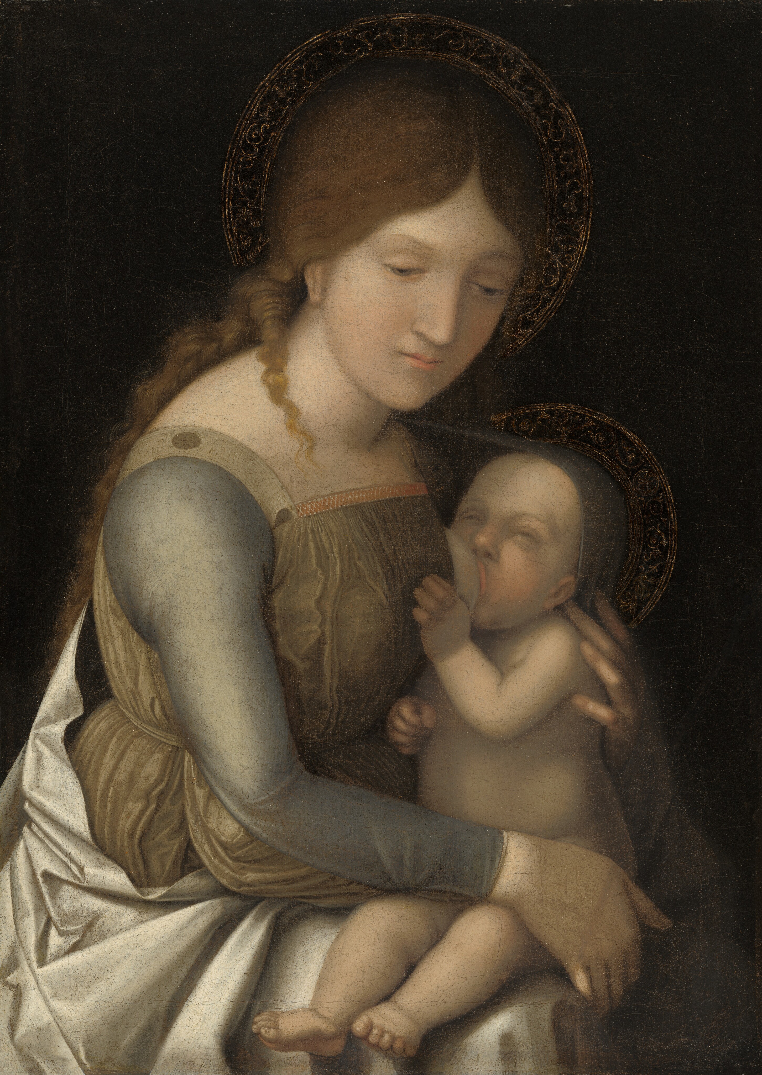 Shown from the lap up, a woman breastfeeds a baby against a dark background in this vertical painting. Both people have gold halos and pale skin. The woman sits to our left with her body angled to our right almost in profile. Her head tips forward, and she looks down from under thin brows. She a straight nose and a pointed chin, and her small pink lips are closed. Her light brown hair is parted down the middle and falls down her back. One curly lock lies over the shoulder closer to us. Her sage-green bodice has a straight neckline and muted blue sleeves. A white cloak falls from her far shoulder, across her back, and across her lap. She holds the baby’s shoulders with one hand, the middle finger lying delicately across one tiny shoulder and resting behind his ear. She braces his backside with the other. He feeds from her left breast, farther from us, with eyes nearly shut in upward-curving slits and upper lip rolled back. He touches her chest with one hand, and his other fist is tucked between their bodies. A piece of blue cloth stretches from her far shoulder to wrap around the back of his head and falls down his back. Their halos are gold filigree against the dark background.