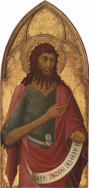Shown from the hips up, a bearded man wearing a textured shirt under a cranberry-red robe stands in front of a gold background in this vertical painting, which comes to a pointed arch at the top. The man’s pale skin has a green-gray cast in the shadows, but his cheeks are pink. His body faces us, but he looks off to our right with slitted, brown eyes under curving brows. He has a long, straight nose and his lips are closed. His shoulder-length brown hair curls around his head, and his beard falls to his chest in long ropes like thick fringe. His textured shirt is topaz blue, and the red robe is edged with gold. He holds his right arm, to our left, so it crosses his chest as he points to our right. A scroll in the other hand reads, “ECCE AGNUS DEI.ECCE Q.” A patterned halo is punched and incised into the gold background. Molding creating a three-lobed shape over the man’s head is punched with dots and marquis-shaped designs. Areas of brick red show through some areas of the gold background.