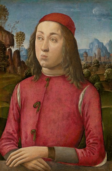 This painting shows a young person from the waist up, sitting with their hands folded on a brown surface. The person is angled slightly to the left, looking up into the distance. They have pale skin, soft, rounded facial features, and long, wavy light brown hair. They wear a vibrant red garment with green ties down the front and a red cap on their head. In the background, there are rocky blue and brown cliffs, tall leafy green trees, and tall gray buildings and towers under a clear blue sky.