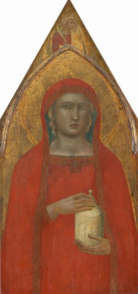 Shown from the hips up, a woman holds an ivory-white, cylindrical jar against a gold background on a panel shaped to come to a sharp point at the top of this vertical painting. The pale skin of the woman is faintly tinted with green. Her body faces us, and she looks at or past us with wide, hooded, light brown eyes under faint brows. She has a long, straight nose, and her pink bow-shaped lips are closed. The woman wears a tomato-red mantle that covers her head and drapes down past her shoulders and over her matching dress. Locks of blond hair show under the mantle on the sides of her face. Bands of geometric designs made with black lines decorate the edges of her mantle and the neckline of her dress. The woman holds her left hand under the jar and her right hand holds onto its peaked lid. A disk-like halo with a floral pattern is incised into the gold background behind the woman. Above the woman, narrow molding affixed to the panel creates a rounded but pointed arch set under the sharp point at the top of the panel. Between the arch and the triangular tip, an angel with harvest-gold wings and blond hair is shown from the chest up. The angel’s body faces us but the head is in profile to our right. A narrow palm frond is held by one shoulder, and a butter-yellow cloth drapes over a cardinal-red gown. The surface of the painting is cracked and chipped, especially in the gold areas. 