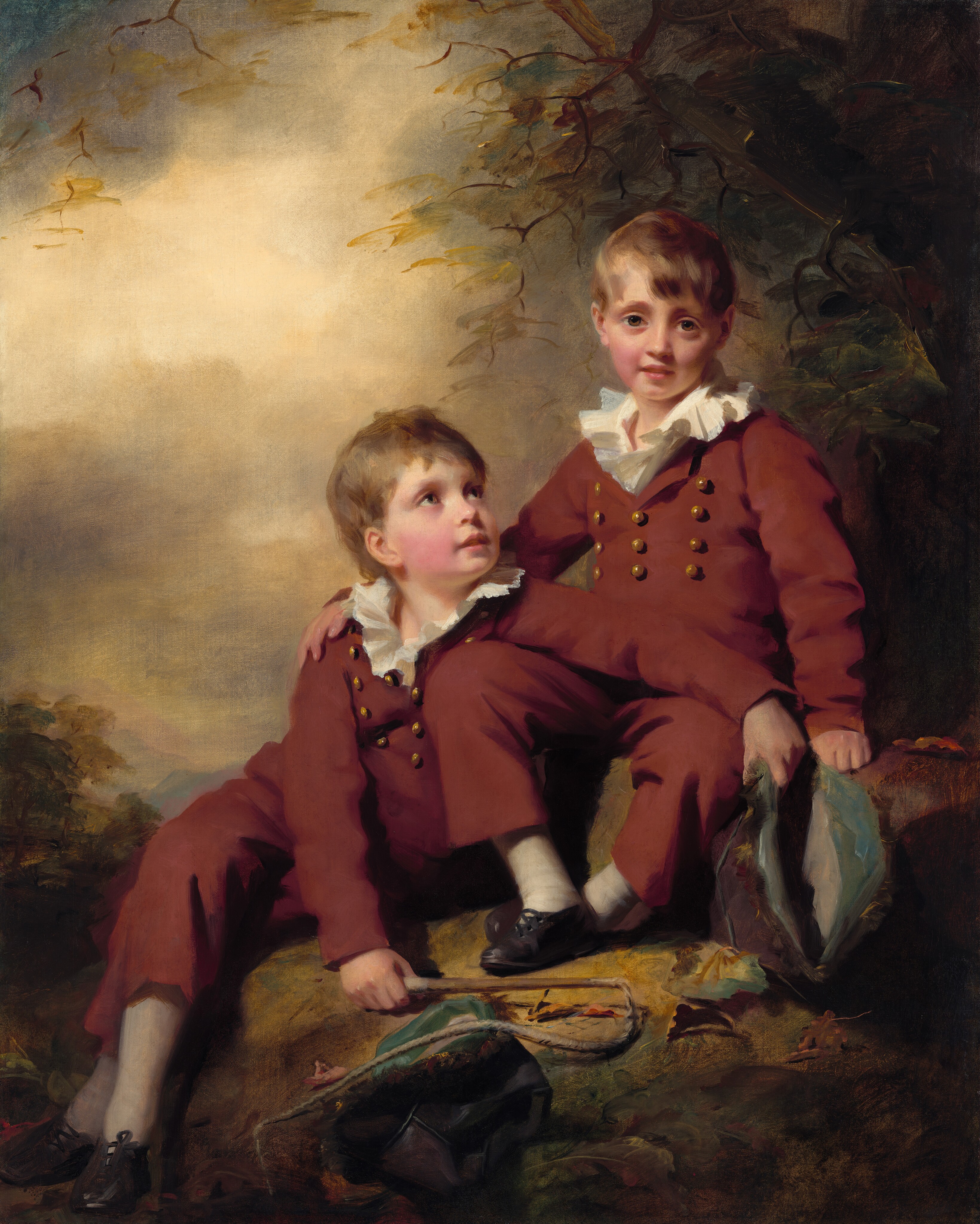 Two young boys sit side by side on some boulders with a cloudy sky behind them and dark tree branches above in this vertical portrait painting. The boys both have pale skin with flushed, round cheeks, short, light brown hair, and brown eyes. They wear matching russet-brown suits with rows of gold-colored buttons on their chests and white ruffles that pop out of their collars, white stockings, and black, laced up shoes. The boy on our right looks at us with his right hand on the other boy’s shoulder. That second boy sits on a lower rock and looks up at the first while draping one arm over the first boy’s lap. The second boy holds a plum-purple and powder-blue hat in one hand and a stick with a rope attached, perhaps a whip, in the other. Another hat lies on a boulder under the rope. A few crisp sage-green, deep yellow, and brown leaves have fallen to the ground at the boys' feet. The tree above and distant landscape beyond are loosely painted in hazy tones of yellow, smoky green, brown, and slate blue.