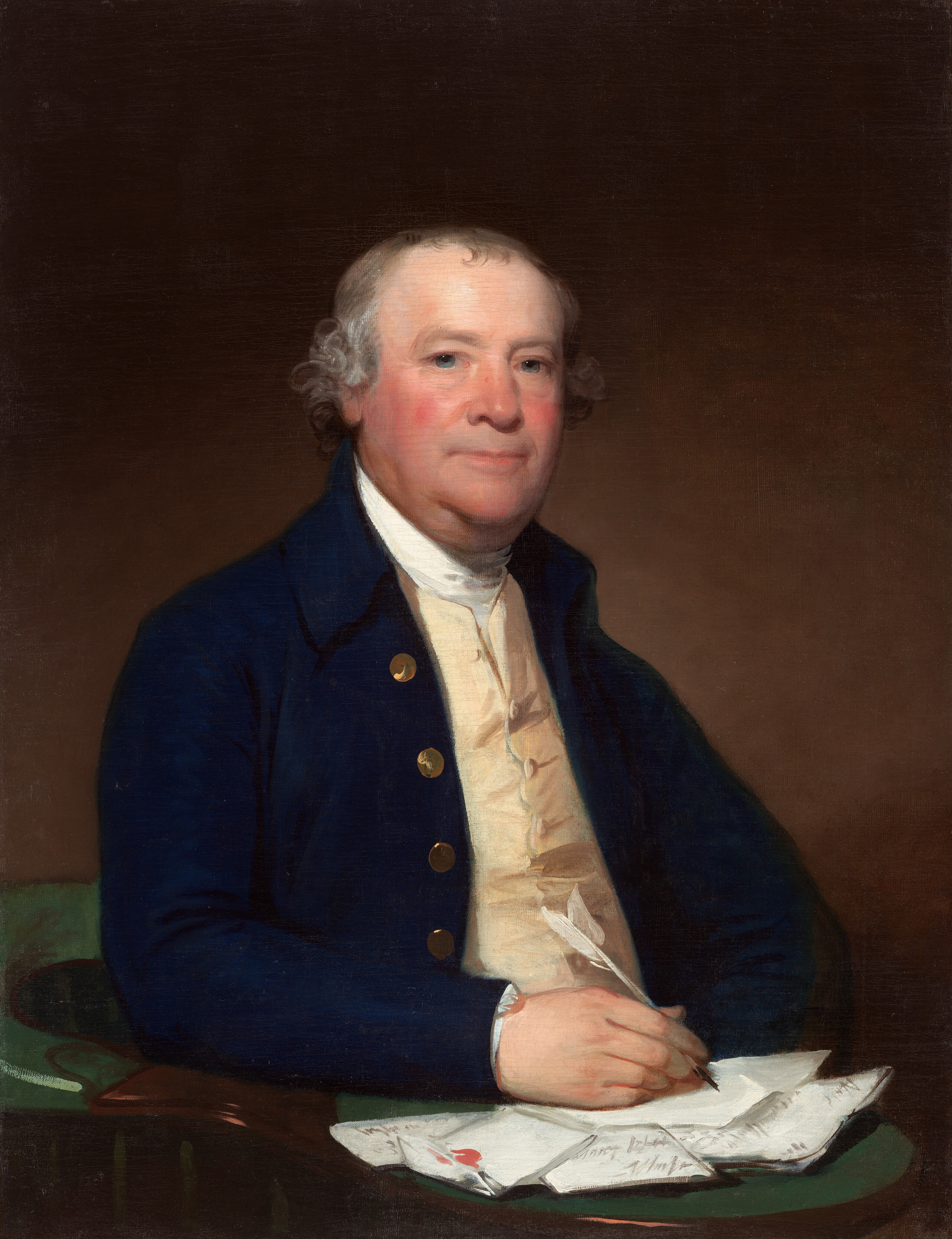 This painting shows a seated man from the waist up, his body turned slightly to the right and his head facing us. He has a round face with fair skin, rosy cheeks, and short, gray hair that curls around his ears. His thin lips are in a neutral expression. The man wears a dark blue coat with gold buttons over a white, high-collared shirt and a cream-colored vest. In his right hand, he holds a white quill pen. His right arm is resting on a green-topped table or desk that is covered with a pile of folded letters or papers, one of which he seems to be writing on. The background is plain and dark brown.