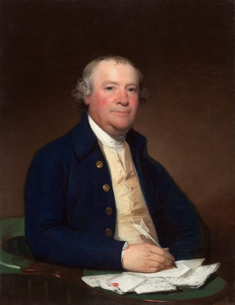 This painting shows a seated man from the waist up, his body turned slightly to the right and his head facing us. He has a round face with fair skin, rosy cheeks, and short, gray hair that curls around his ears. His thin lips are in a neutral expression. The man wears a dark blue coat with gold buttons over a white, high-collared shirt and a cream-colored vest. In his right hand, he holds a white quill pen. His right arm is resting on a green-topped table or desk that is covered with a pile of folded letters or papers, one of which he seems to be writing on. The background is plain and dark brown.