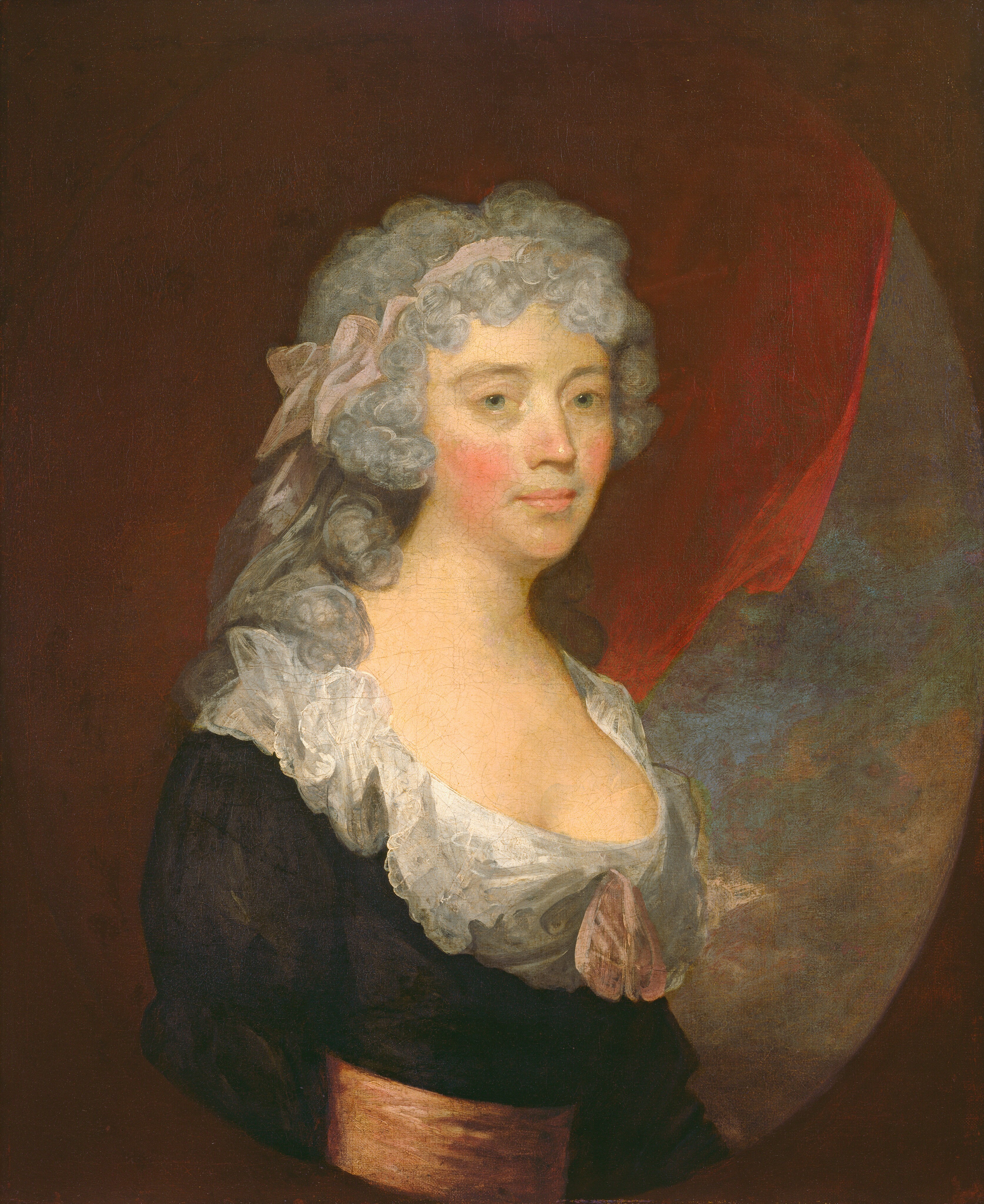 This painting shows an upper body portrait of a woman with her body slightly turned to the right and her head facing us. She has light-colored skin, rosy cheeks, green eyes, and pink lips set in a neutral expression. Her curly gray hair is tied with a light pink ribbon. She wears a dark dress with a low neckline lined with lace and a pink bow at the center, and a light orange-pink sash around her waist. Behind her is a dark red curtain on the left, and a blue sky on the right, covered in brown and gray clouds. The portrait is enclosed in an oval which is set against a dark brown background.