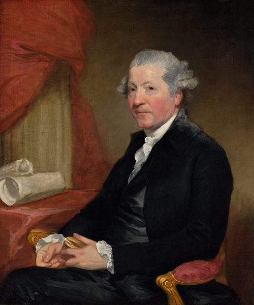 This painting is a portrait of a man shown from the waist up. He is seated, facing slightly to the left but looking directly at us. The man has light gray hair styled back from his face, with curls visible at the sides. His skin is fair with slightly pink cheeks. He is wearing a formal outfit: a dark jacket over a white, high-collared shirt with ruffled edges and dark trousers. He holds a small object, possibly a box, in his hands, which are placed in his lap. There is a red cloth or curtain behind him, with rolls of parchment or cloth on a table nearby on the left. The wall behind him is a muted green color that fades into shadow near the upper-right and lower-right corners.