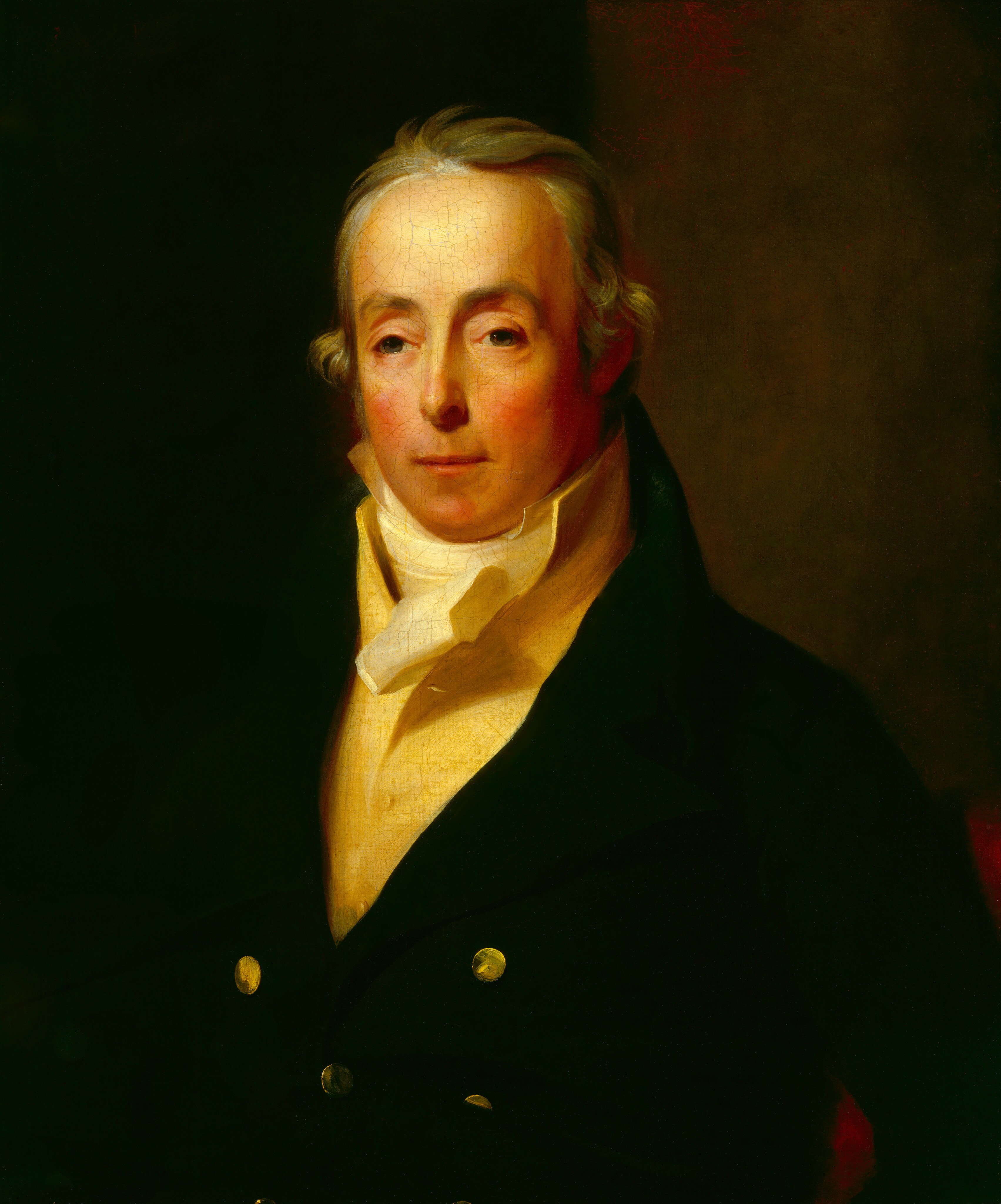 This painting is a portrait of a man from the waist up. He is facing us, with pale skin, thin lips, rosy cheeks, light green eyes, and gray hair styled into curls around his ears. He has a neutral expression. The man is wearing a dark coat with gold buttons on the front, with a pale-yellow shirt underneath and a white cravat around his neck. The background is a dark and indistinct brown color.