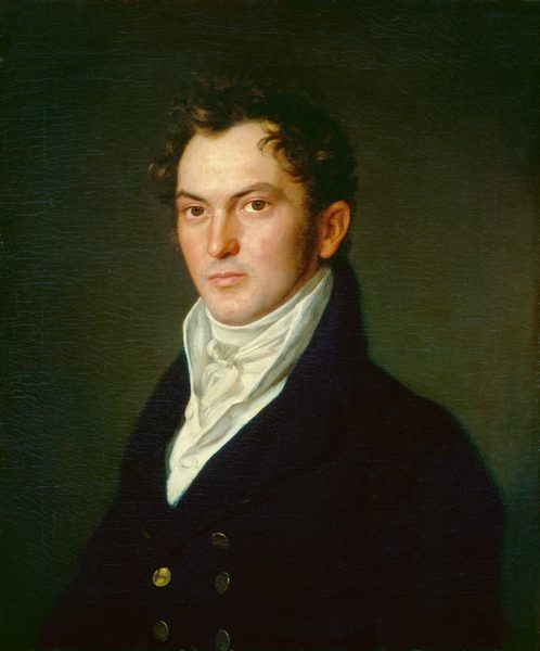 The image shows a man depicted from the waist up, positioned slightly turned to the side yet facing the viewer directly. He has a composed expression with defined facial features, including a high forehead, strong eyebrows, prominent cheekbones, and a clean-shaven face. His hair is dark and curly, styled away from his forehead. He is dressed in a dark coat featuring a double-breasted design with gold buttons, complemented by a high-collared, white cravat intricately tied at his neck. In the background, there is a subtle, dark, greenish hue.