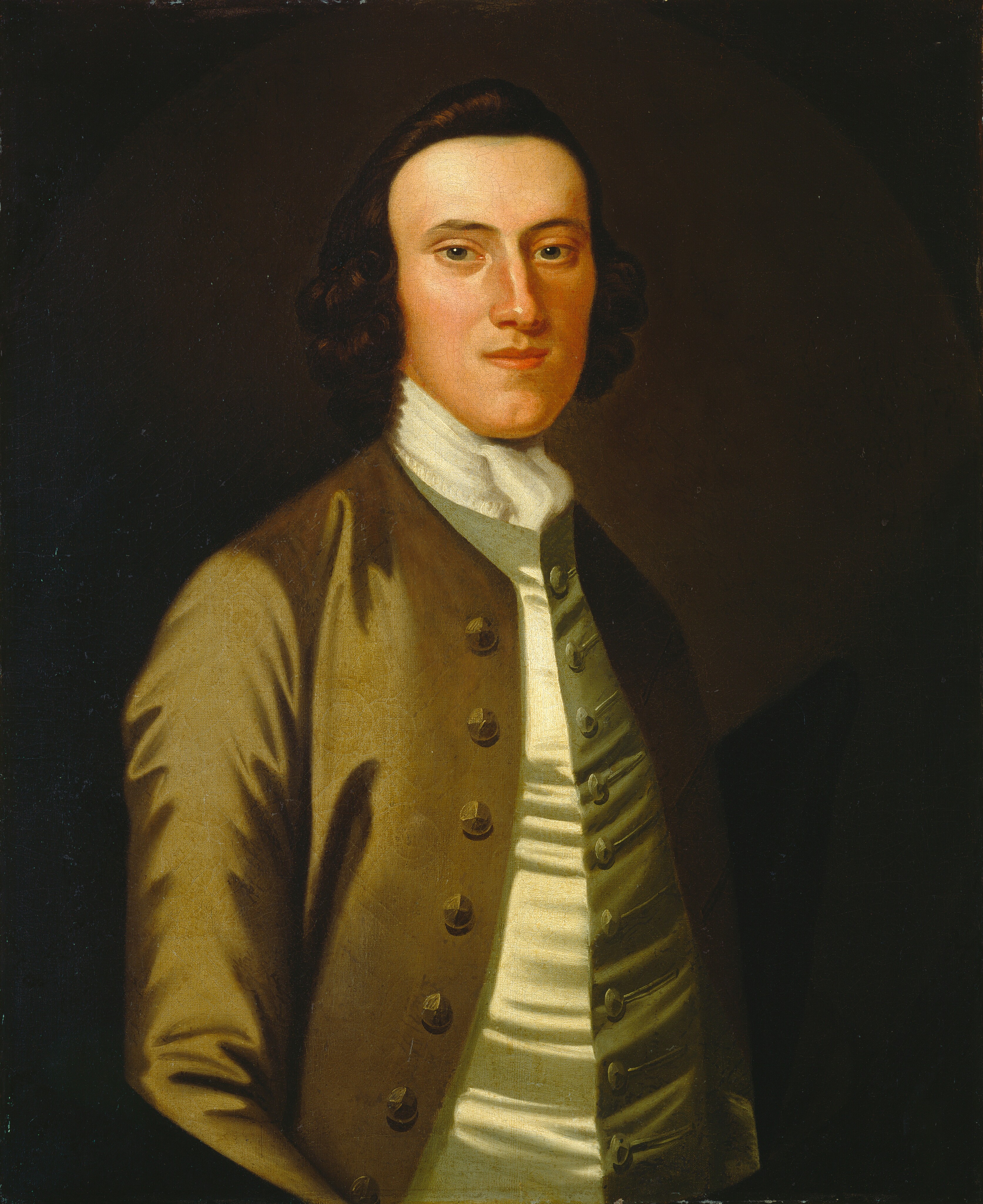 The image displays a painted portrait of an individual, showing the upper half of the body prominently. The person is positioned facing slightly toward the viewer's left with their gaze directed forward. They have defined facial features with a smooth complexion and medium-length, curly brown hair that frames their face. The attire consists of an elegant coat with distinct buttons and a high-collared shirt underneath. There is a subtle shine and texture to the clothing. There are no visible jewelry pieces, and the person is not holding any objects. The background is a dark, neutral color, contrasting with the lighter tones of the person's skin and clothing.
