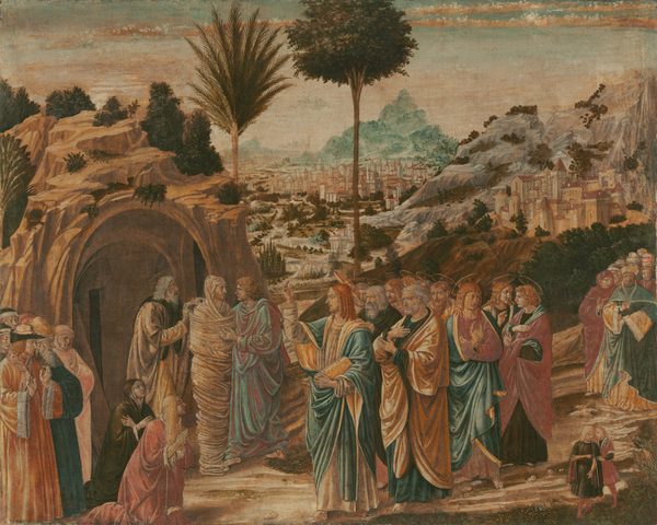 This is a painting of a group of people gathered around a cave-like structure in a hilly landscape. The people have light skin and wear ornate and flowing robes in shades of pink, teal, and gold, and they are gathered closely together, some gesturing towards the cave. At the mouth of the cave, a man wrapped in strips of off-white cloth stands, looking out at the crowd. Two other men stand next to him, appearing to remove his cloth wrappings. To the right, in the center of the image, a man with long golden hair faces the cave and raises one arm. He wears blue and gold robes over a white garment, and his other hand holds a golden book. There is a halo behind his head. Behind him are ten other men of varying ages wearing colorful robes who also have halos. In the background are hills, greenery, and a sprawling city of white buildings with red roofs that extend towards the horizon. Tall palm trees punctuate the landscape, and the sky above is light blue with pink clouds.