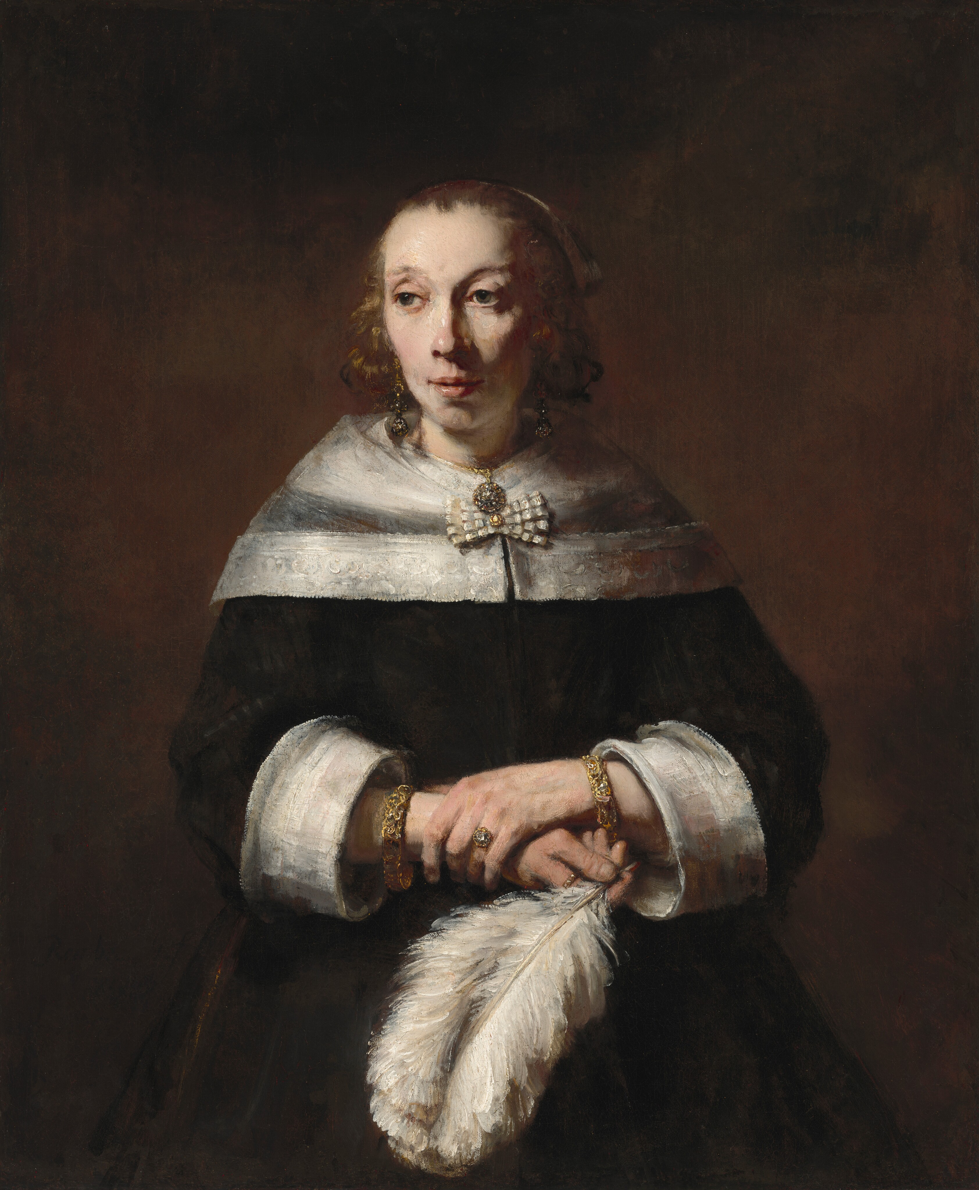 A woman with pale skin, wearing a black dress and holding a full, billowing white ostrich feather, is shown from the hips up against a dark background in this vertical portrait painting. She has dark eyes, faint, arched brows, a slightly pink nose, and her pink lips are parted. Light falls from our left, creating shadows under the other cheekbone and along the side of her neck. Her shoulders are covered by a transparent, white, lace-edged wrap fastened with a bow. Her black dress also has wide, white cuffs, exposing a thick, possibly jeweled bracelet on each wrist. She wears two gold rings, one with a clear gem, perhaps a diamond, gold, dangling earrings, and a round pendant necklace. The lush white ostrich feather arches down from her right hand, held at her waist by her opposite hand, clasping that wrist.