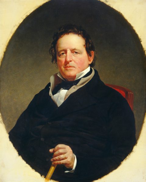 The painting depicts a man shown from the waist up, seated and facing forward. He has a sturdy build and is positioned with a relaxed posture. His facial features include a fair complexion, a slightly flushed tone, and a solemn expression, with round cheeks, deep-set eyes, and a strong jawline. His dark hair is short and somewhat tousled, framing his face. He is dressed in formal attire consisting of a dark coat over a white shirt with a high collar, a gray cravat around his neck. His right hand is resting on his lap, holding a cane, and a gold ring is visible on his finger. The background is plain with a muted color, and is set within an oval frame.