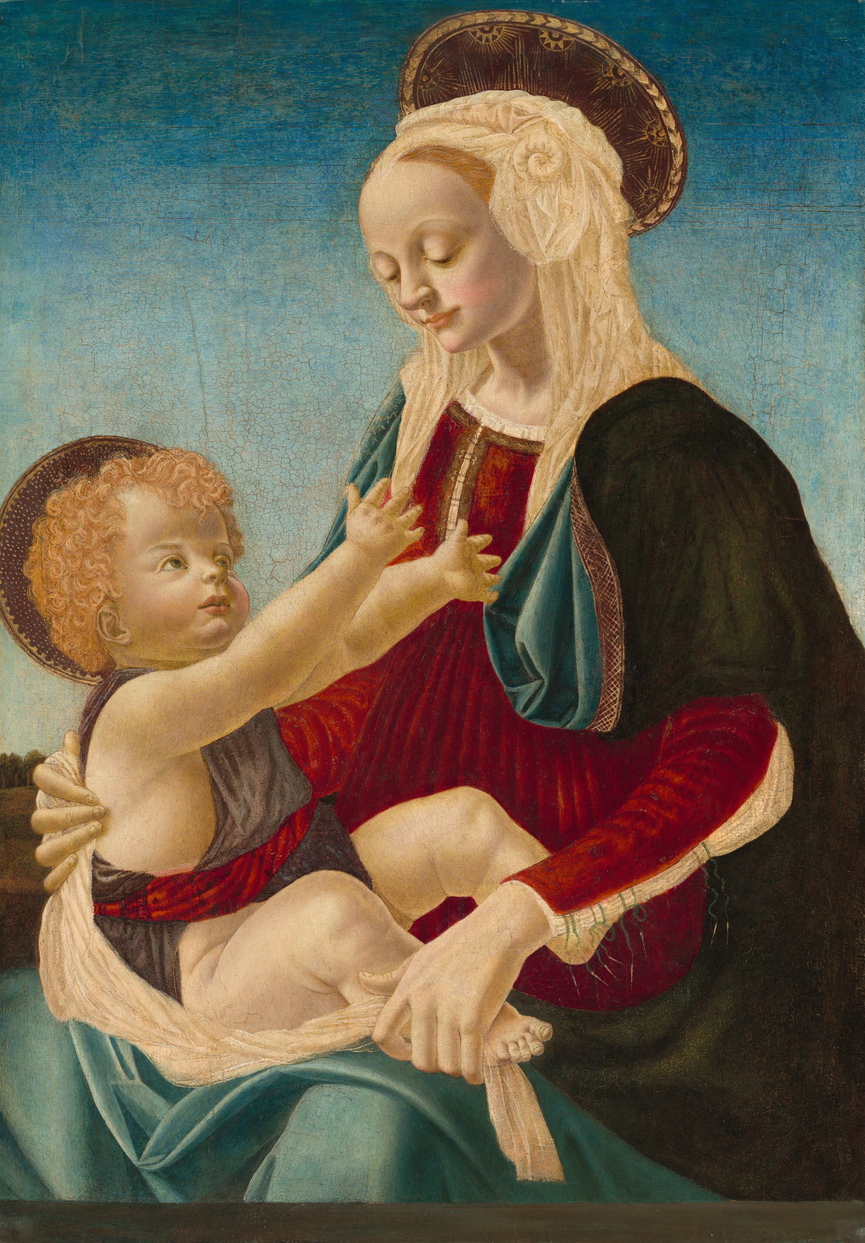 Shown from the knees up, a woman holds a baby in her lap in front of a clear blue sky in this vertical painting. The woman and baby both have smooth, pale skin with rosy cheeks and flat, disk-like halos at the backs of their heads. The woman’s body is angled to our left, and she looks down and smiles faintly at the baby she holds on her lap. Her blond hair is mostly covered by a gathered and ruffled white headdress. Her forest-green robe is lined with topaz blue, and it falls over her shoulders and across her lap over a ruby-red, long-sleeved dress. The white garment beneath the dress is visible along an open seam down the arm we can see, and the front of the dress is pleated vertically from the high waist. The woman supports the baby’s back with one hand and one of his feet with her other. He has curly blond hair, round cheeks, and delicate features. He reaches for the woman with both chubby hands. A slate-blue cloth drapes over his shoulders and is tied with twisted red fabric. A gray band across the bottom of the panel suggests they sit on the far side of a stone ledge. A ridge of trees along a hill in the deep distance is visible along the left edge of the composition, and the sky above deepens from watery blue along the horizon to azure blue across the top. The surface of the painting is cracked in some areas, especially in the sky.