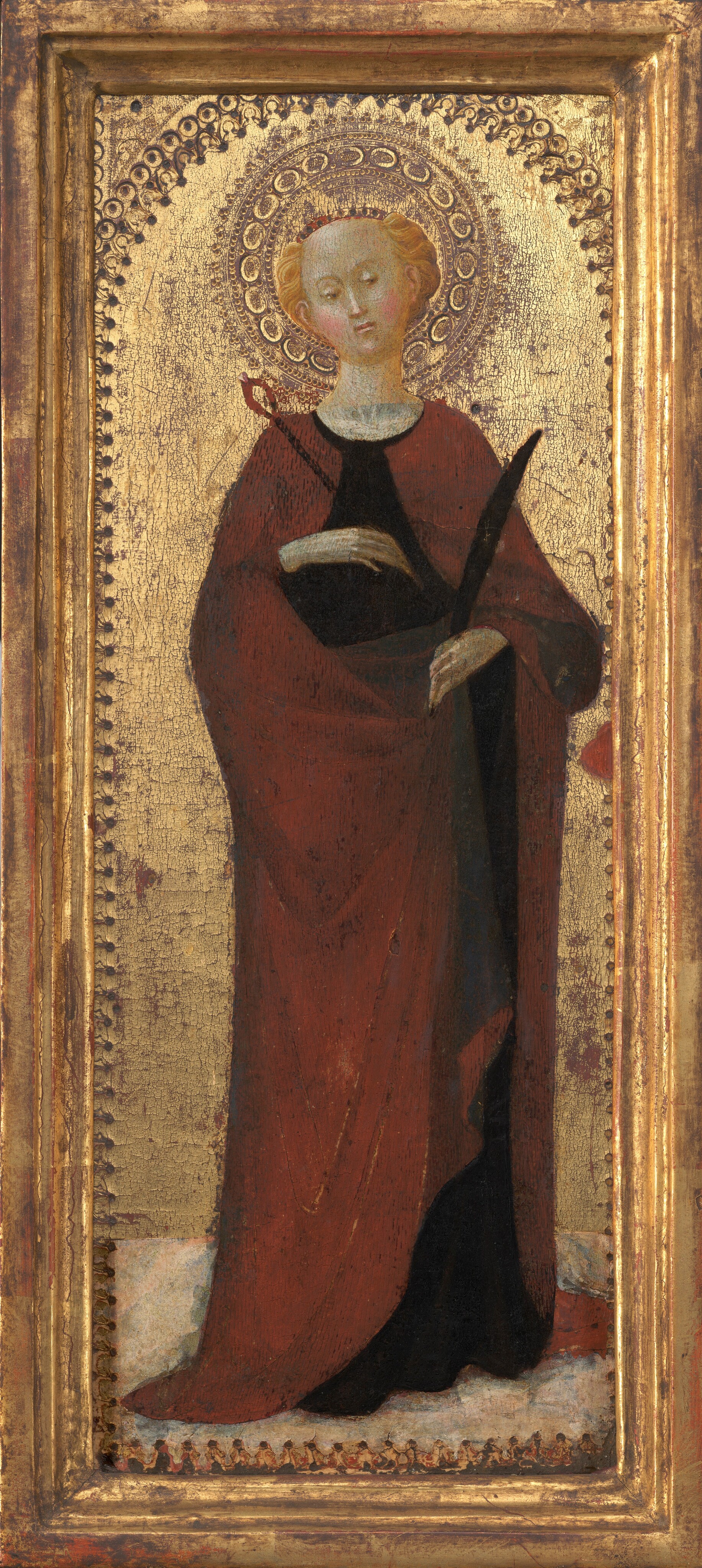 This painting shows a person standing, their head slightly tilted to the left. They have a pale complexion, and short, wavy blonde hair adorned with a thin red crown. They have rosy, pink cheeks, arched eyebrows, a straight nose, and small lips set in a neutral expression. The individual is wearing a long red robe over a black tunic or dress and is holding a long black quill-like object in one hand, and what looks like a thin staff with a red loop at the end in the other. A detailed golden halo surrounds their head, and the background features an ornate gold pattern which is slightly worn and peeling in some places. The painting is bordered by a golden frame.