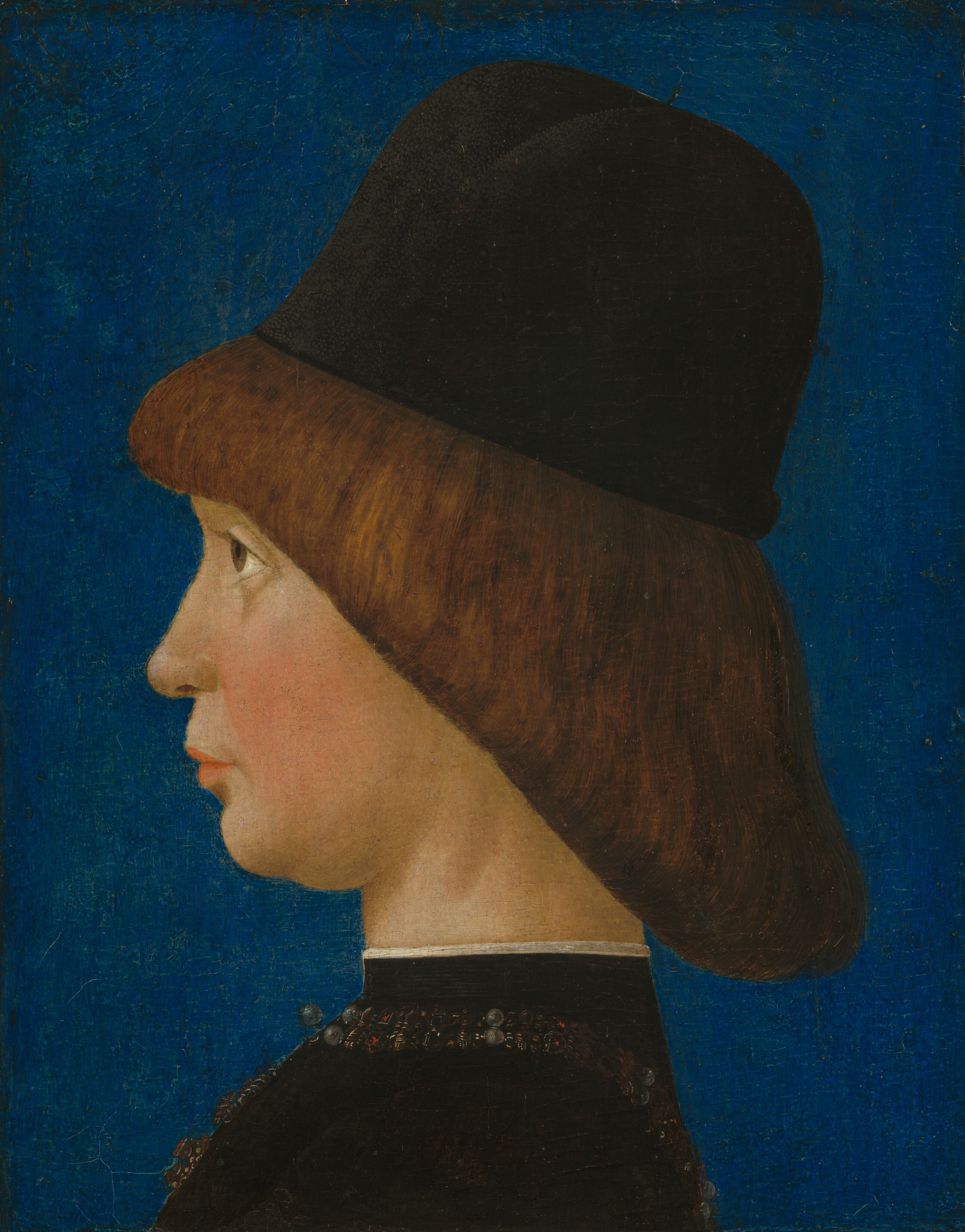 Shown from the shoulders up, a pale-skinned boy faces the left in profile against a lapis-blue background in this vertical portrait painting. He stares steadily forward with brown eyes, rosy cheeks, and closed pink lips. His chin is pulled slightly down and back. The boy's brown hair falls from bangs across his forehead in a straight, diagonal line to the nape of his neck. He wears a brimless black cap with a high, rounded crown. His high-necked, black garment has gold, black, and pearl embellishments around the neckline and down the front. The collar is edged with white along the top.