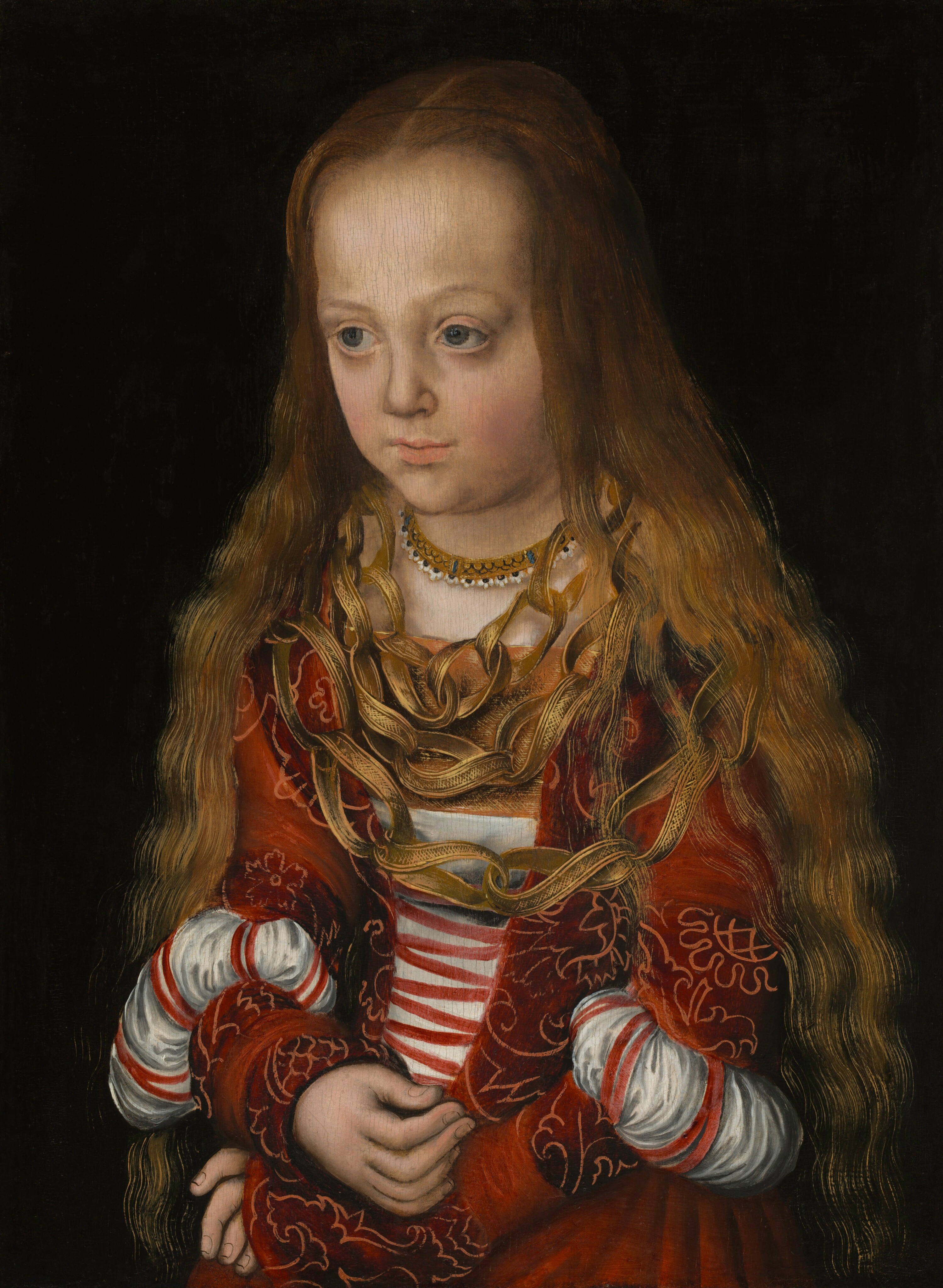 Shown from the lap up, a young girl with pale, peachy skin and long, light brown hair wears a crimson-red dress with slashed, puffed sleeves and three large, gold-colored necklaces covering much of her chest in this vertical portrait painting. She sits with her body angled slightly to our left and, with her head tipped slightly forward, she looks off in that direction with slate-blue eyes under faint brows. Her long, wavy, golden-brown hair falls from her high forehead and lies loose around her shoulders. Her dress has bands of a floral pattern outlined in a lighter red against a ruby-red background, and the bodice ties with red laces down the front over a white undershirt. The tight-fitting, long sleeves are slashed around the elbows so the white linen shirt can be pulled through to create puffs. Her high-necked chemise has a jeweled band at the neck. The three strings of the distinctive necklace seem to be made of gold-colored strips of fabric or leather made into twisting loops, which are then linked together like a paper chain. Each strip is painted or decorated with a fine, dense lattice pattern and edged in gold. The girl sits with her wrists crossed in her lap against a black background.