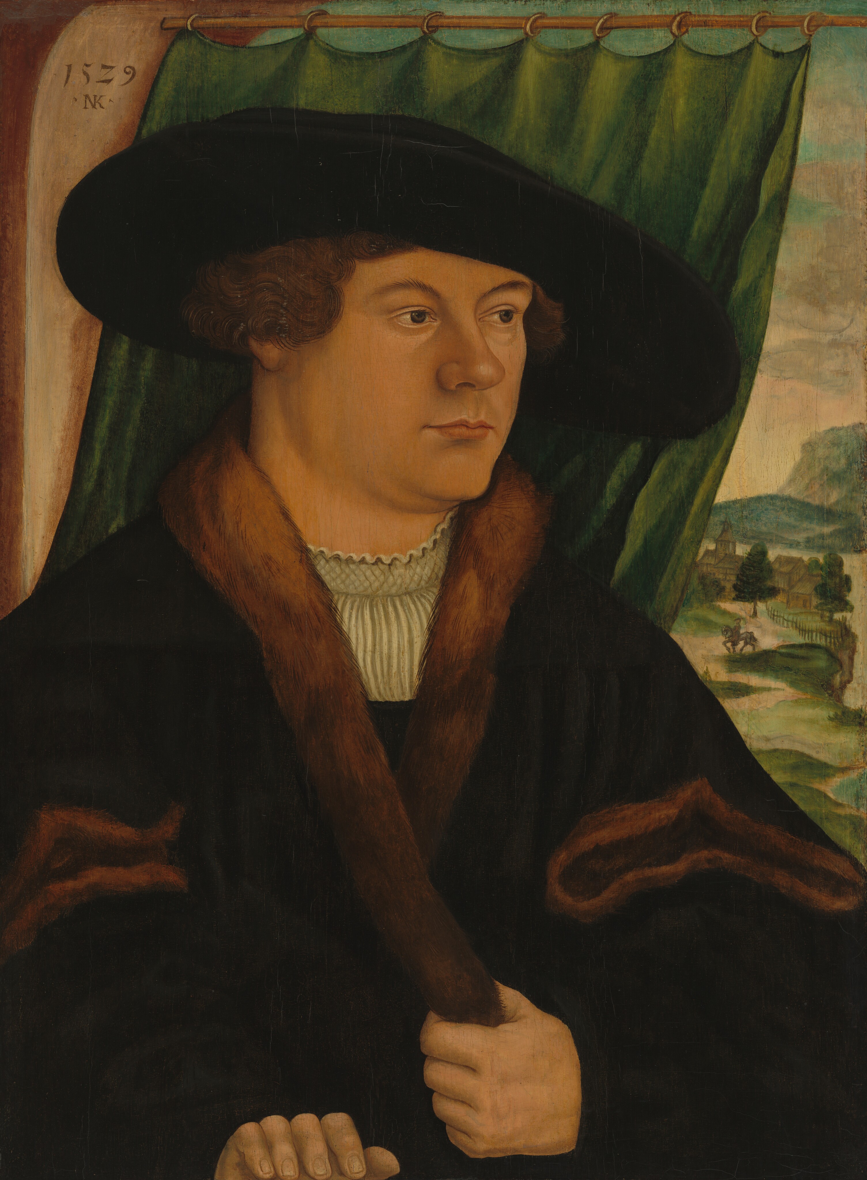 The image depicts a man from the waist up, turned to the side and looking to his right. He has a round face, brown curly hair, and wears a black hat, coat with fur lining, and a white pleated shirt. One hand holds the fur on his coat, while the other rests in front of him. In the background, a green curtain is partially drawn aside, revealing a landscape with a tree, a building, and a faint path or river. The inscription "1529 N.K." is at the top left.