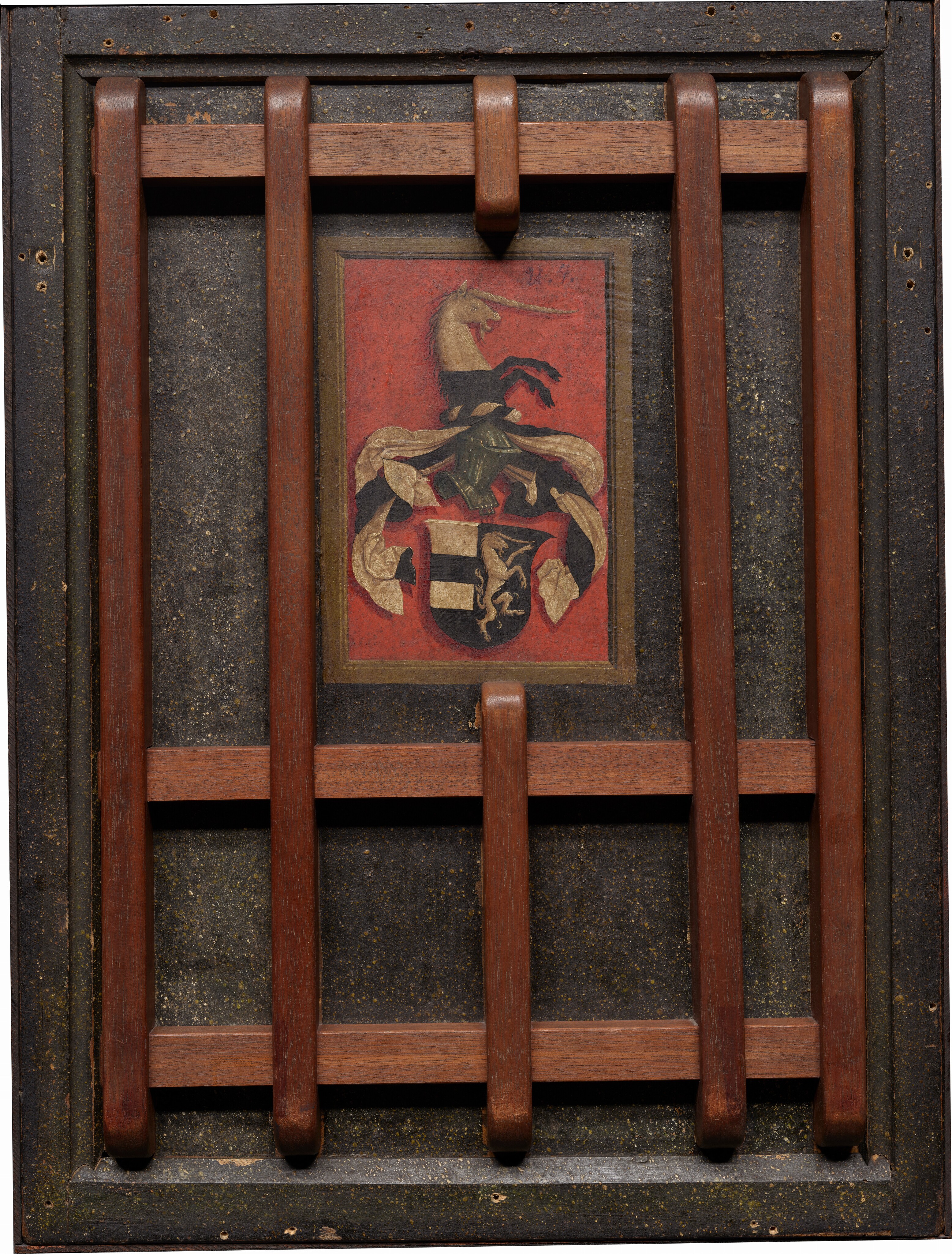 This is a painting depicting a heraldic coat of arms. The image features a detailed coat of arms with a central shield, adorned with black and gold sections, and additional decorative elements above it. There is a figure resembling a unicorn emerging from the crest. The background is a deep red hue. The artwork is displayed within a wooden frame with crossbars. This style is associated with displaying family crests and lineage.
