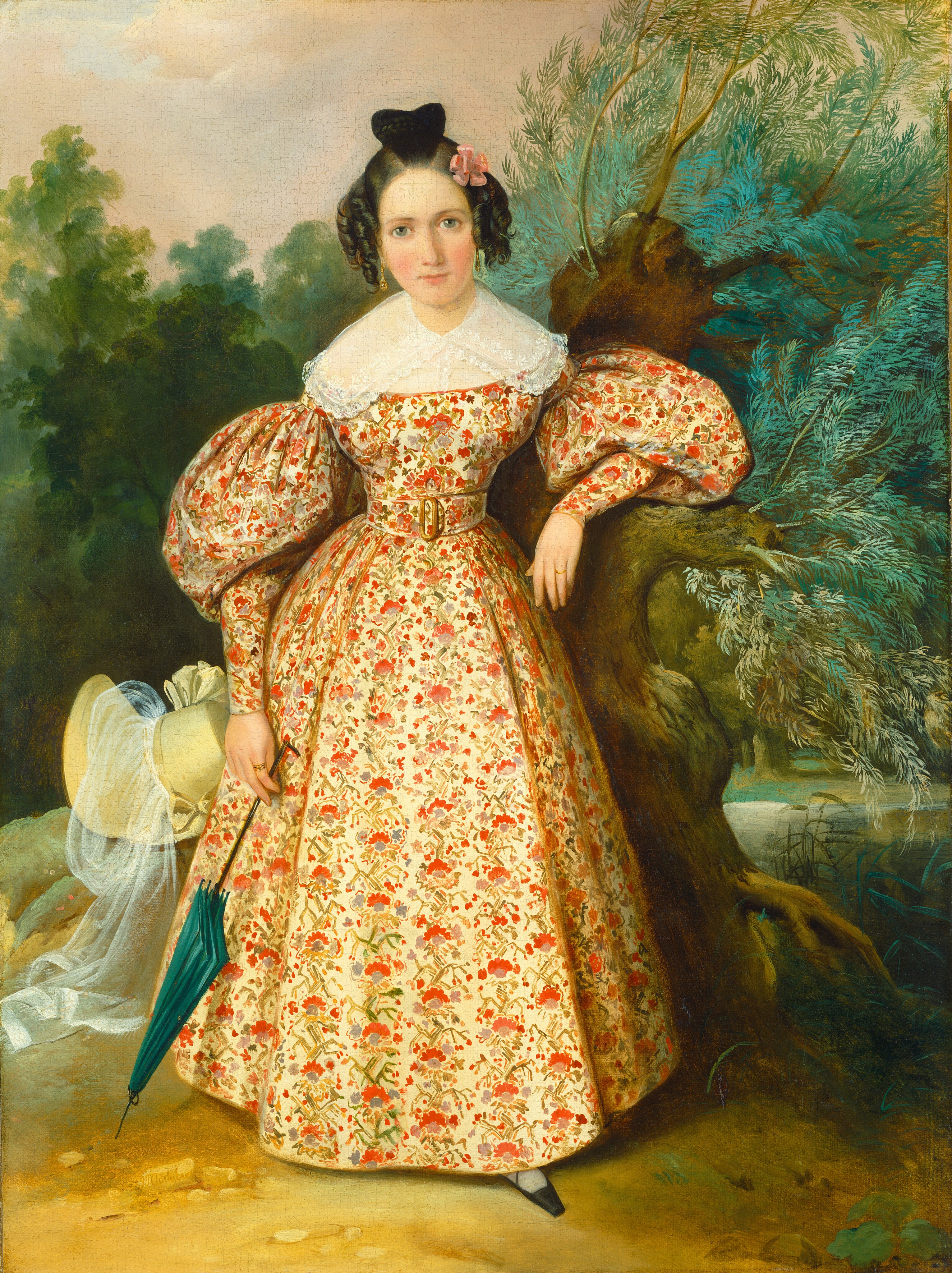 This painting shows a woman standing next to a tree, her left arm resting on a low branch. She has fair skin, rosy cheeks, large eyes, and dark curled hair in an updo and adorned with a pink flower. She wears a dress with a red-and-green floral pattern on a pale-yellow background, puffed sleeves, a lacy collar, and a wide belt. She is holding a closed green umbrella in her right hand. A pale-yellow hat with a veil rests on the ground behind her to the left. She stands on a brown patch of dirt, and to the right appears to be a body of water with green reeds. The background shows dense green trees under a sky of pastel pink clouds, a small patch of blue visible near the top left.