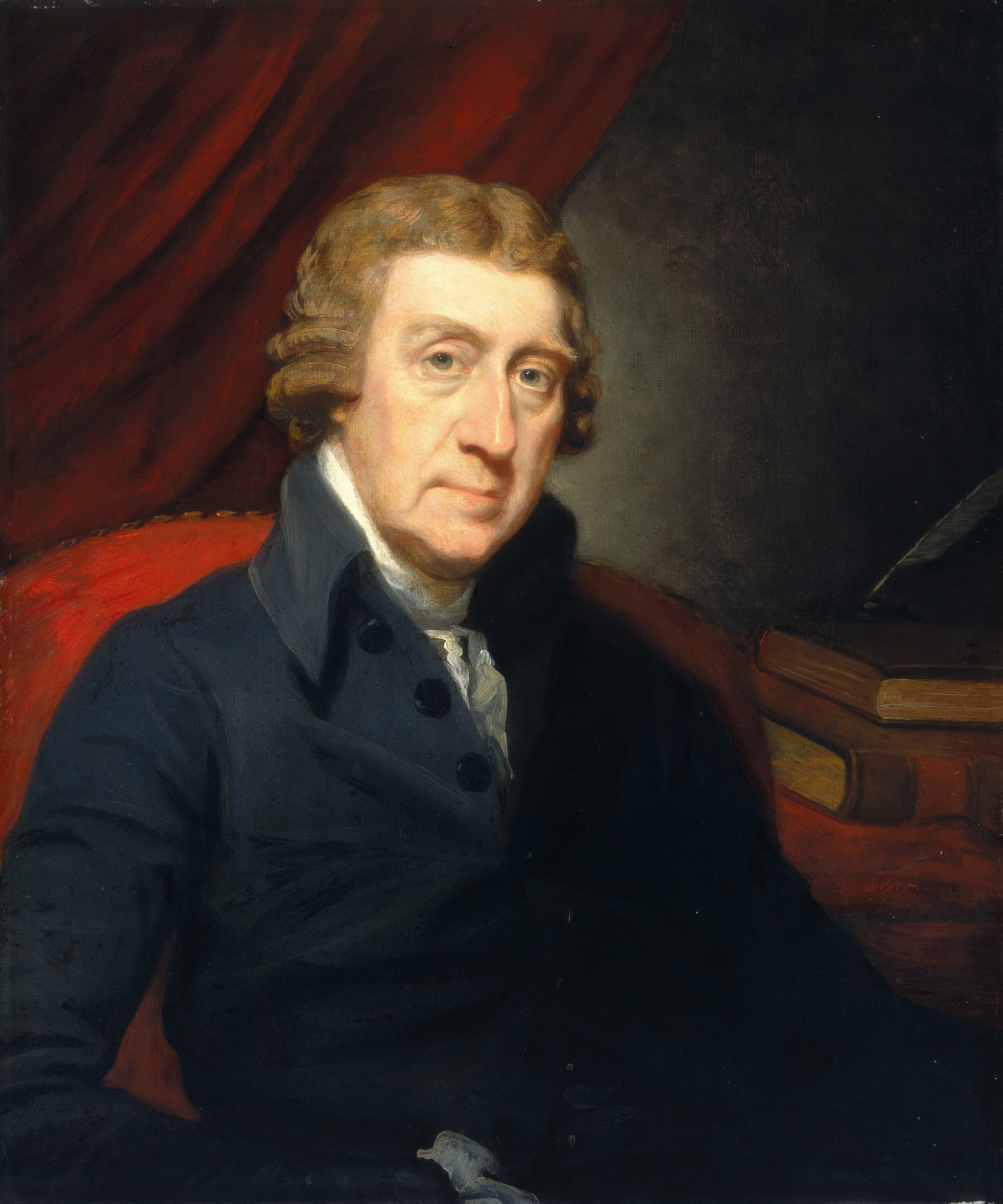 The image shows a man in a dark suit with a white cravat, sitting and facing slightly to his right. He has light brown curly hair, fair skin, light blue eyes, a straight nose, and a subtle smile. The background is a red drapery with books stacked horizontally partially hidden behind it, and the man is illuminated against this backdrop.
