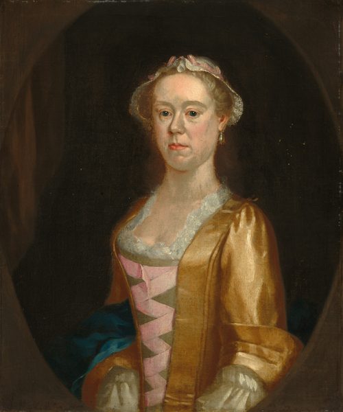 The image displays a portrait of a woman with fair complexion, featuring a distinctive nose and a subtle smile. She has light-colored, neatly styled hair with a ribbon or band. The woman wears a golden-yellow gown with white lace trim and a pink ribbon on her bodice. There is a hint of blue fabric near her waist, and she wears an earring on her left ear. The background is dark, focusing on the woman in the foreground.