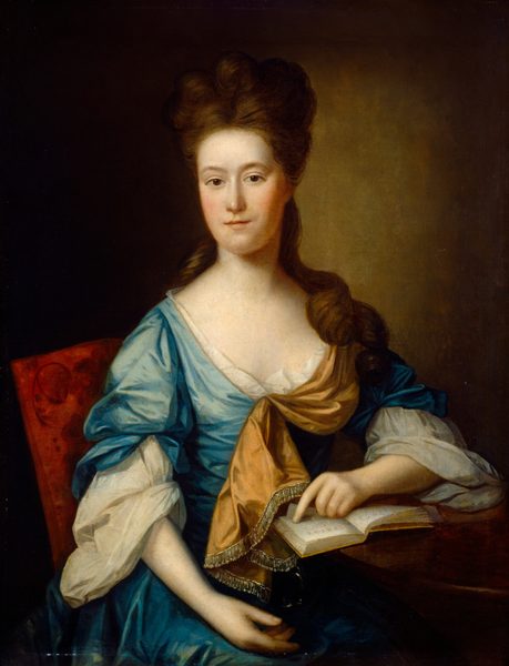 The image depicts a woman seated, facing slightly to the side with her gaze directed towards the viewer. She has soft, delicate skin and a calm expression. Her hair is styled in an updo with loose curls. She is wearing a blue dress with white lace, puffed sleeves, and a golden-orange shawl draped across her chest. She is holding an open book, with one hand resting on a surface. The chair has a red fabric with subtle patterns, and the background is a dark, warm-toned wall.