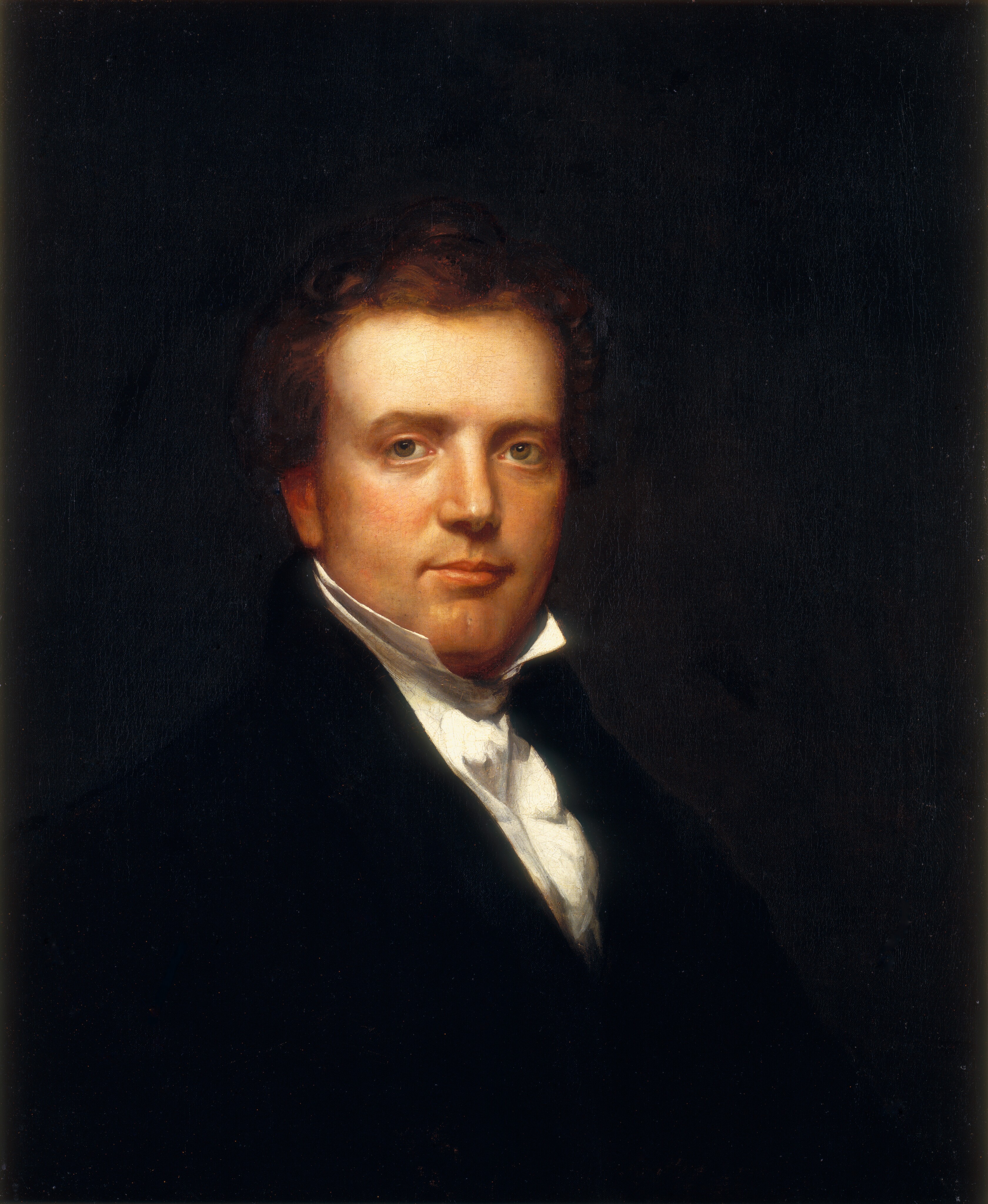 The image is a portrait showing the upper half of a man's body. He is positioned facing slightly to his left while looking directly at the viewer. The man has a fair complexion with soft facial features, including clear eyes and a slight smile. His hair is dark, wavy, and styled with a gentle wave atop his head. He is dressed in a formal black coat over a white shirt, featuring a high collar. The background of the image is a dark, solid color. No jewelry or objects are visible in the painting.