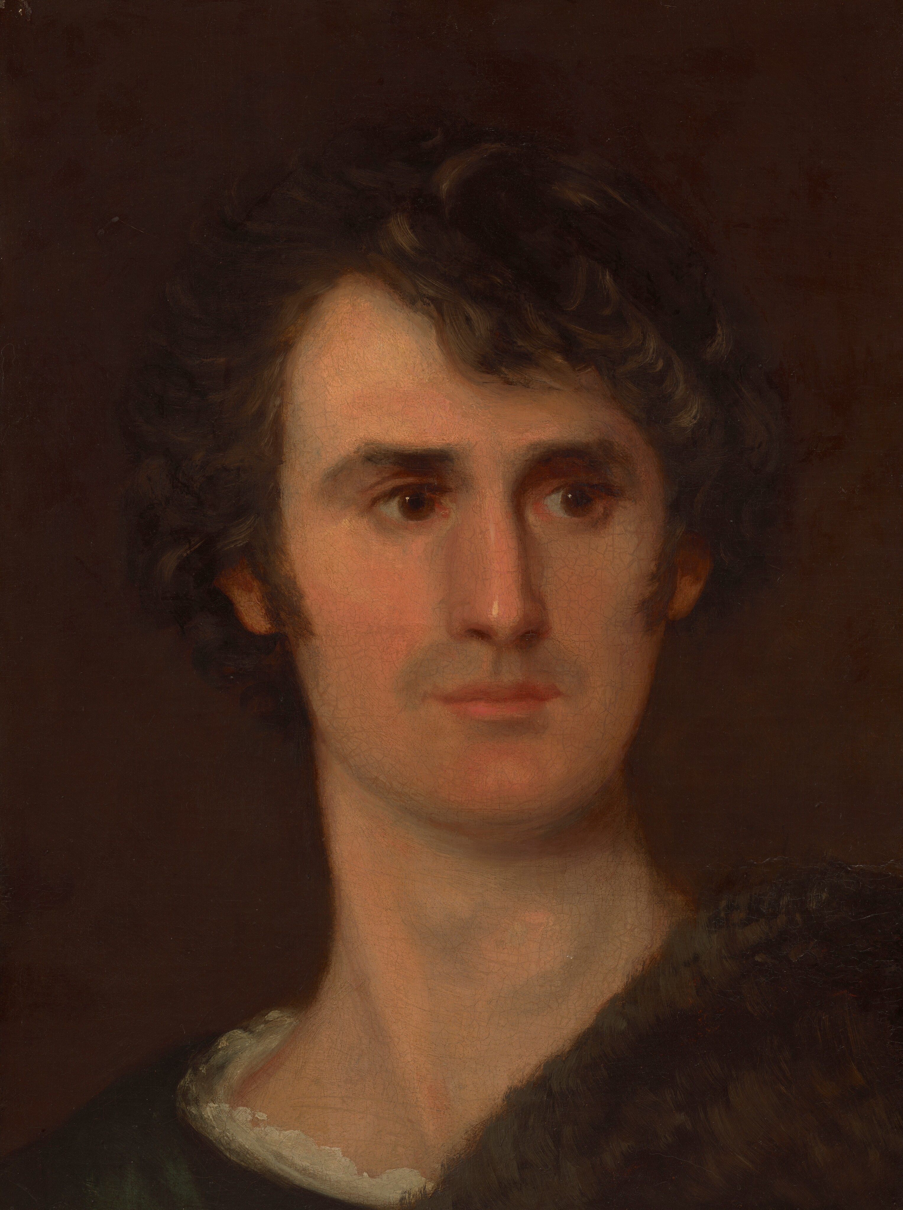 The image is a portrait showing the head and upper part of the torso of a person. The person is positioned with the upper body slightly turned to the side while gazing forward. They have a youthful face with prominent facial features, including deep-set eyes and a straight nose, accompanied by dark, curly hair framing their face. The individual is dressed in a garment that appears to have a dark, textured shawl or wrap over a lighter shirt, visible around the neck area. The background is a plain, dark brown.