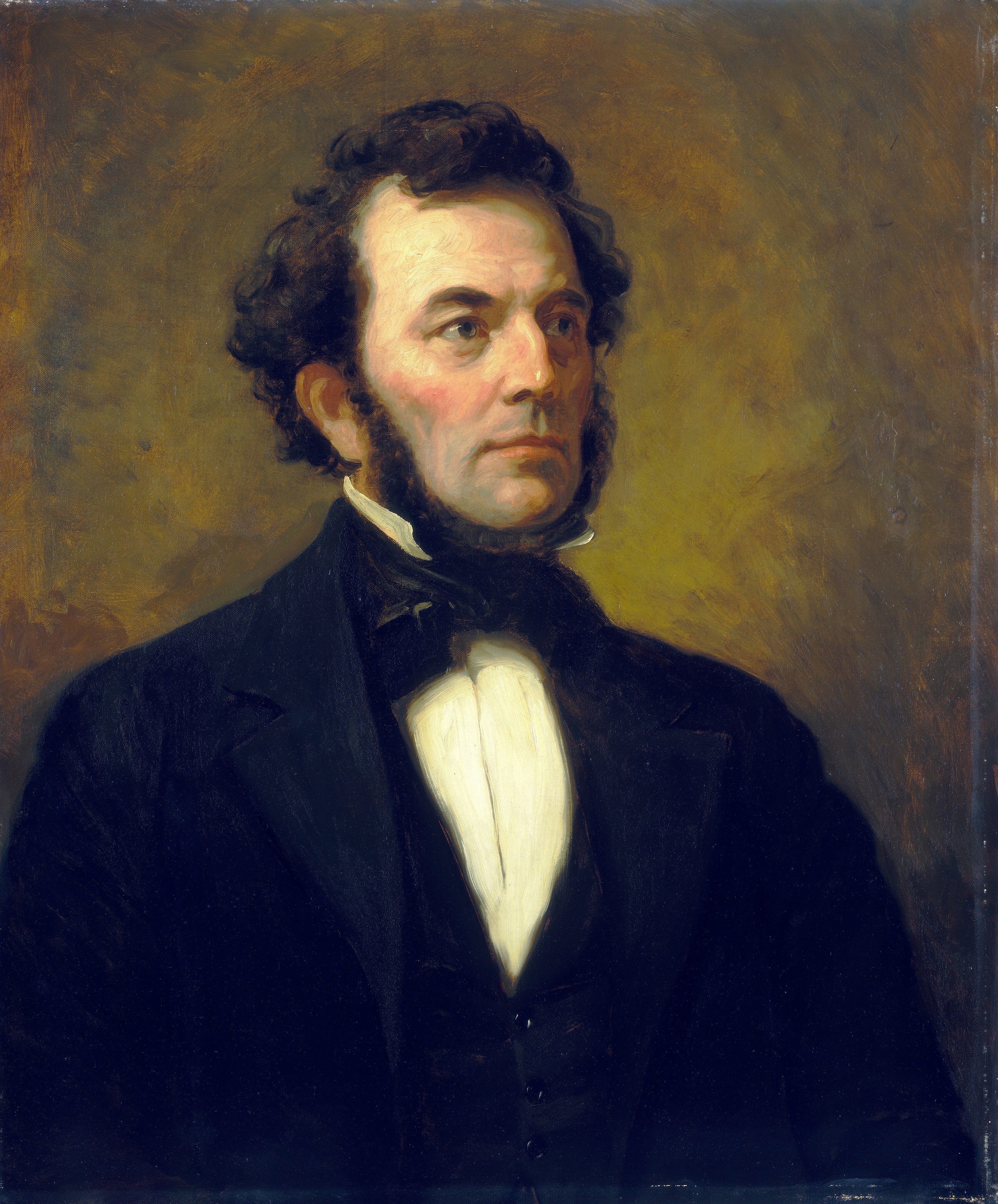 The image depicts a man from the waist up. He is positioned slightly to the side and looking away from the viewer. He has a prominent jawline, large sideburns, and curly, short brown hair. The man is dressed in formal attire, wearing a dark suit jacket over a white shirt with a high collar, potentially with a dark waistcoat and a bowtie. There are no visible jewelry or objects held. The background features a textured mix of brown and earthy tones, creating a neutral and classic setting.