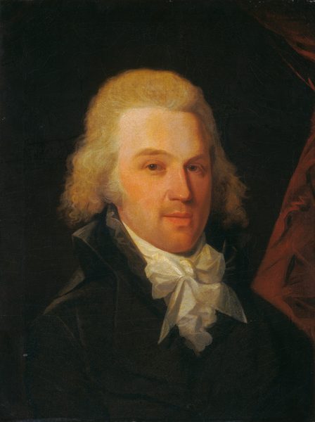The image shows a man with fair skin, blonde curly hair, and facial features including a straight nose and arched eyebrows. He is wearing a dark jacket and a white cravat, against a dark background with a hint of burgundy cloth on the right side. No jewelry or items are visible.
