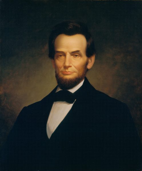 This painting depicts the upper body of a man in a seated position, facing us. He has pale skin, a prominent nose, deep-set eyes, and a neutral expression. His dark hair is styled back, and his dark beard is neatly trimmed. He is dressed in a black suit with a white shirt and a black bow tie. The brown background is lighter near the center of the painting and darker near the edges.