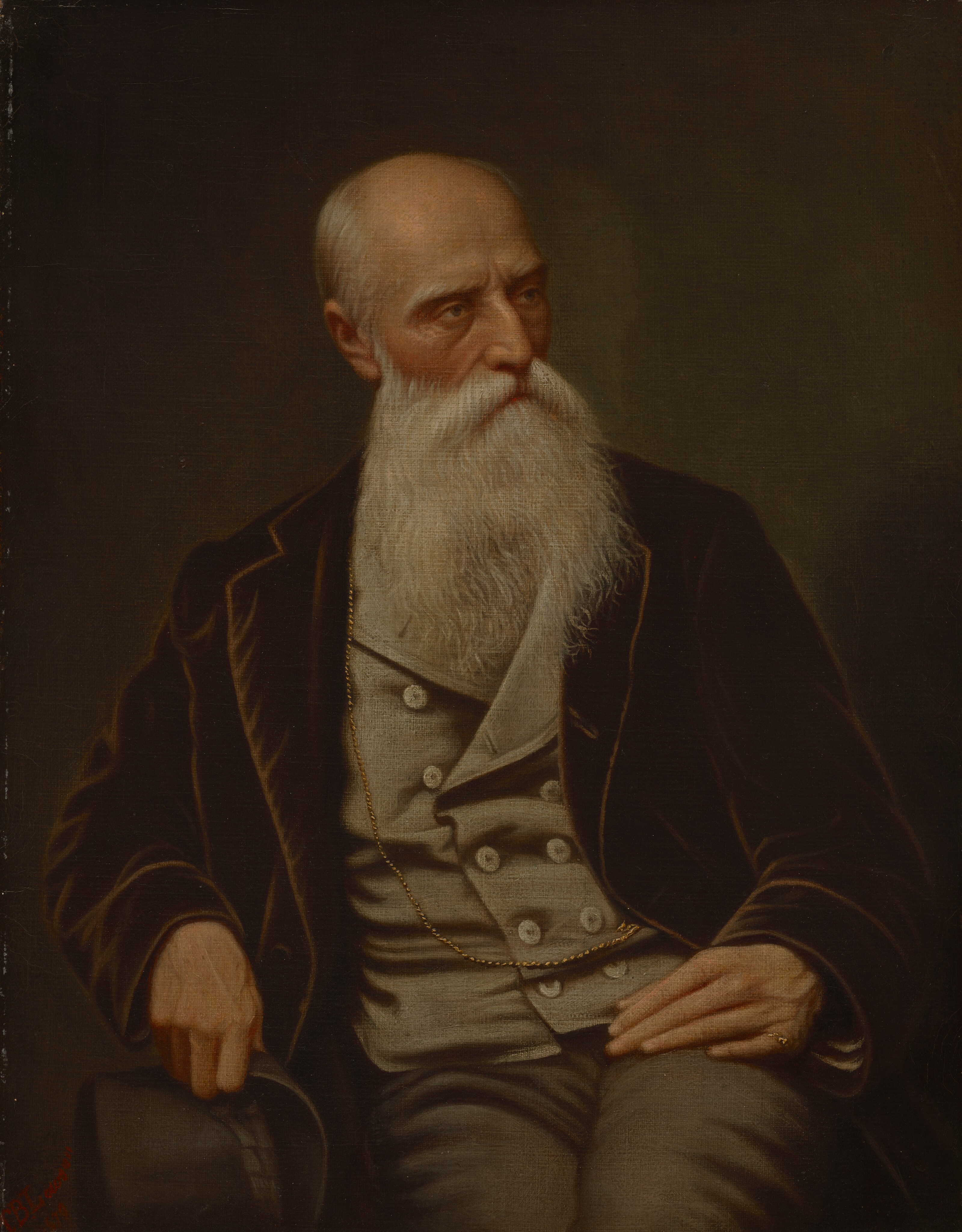 The image depicts a seated man from the waist up. He is facing slightly to his right and looking to his left. The man has a long white beard, closely shaven hair, deeply set eyes, and a slightly furrowed brow. He is wearing a black jacket over a grey waistcoat and trousers. A gold chain is visible around his neck and tucked into the waistcoat. He has a ring on his left hand and is holding a black top hat with his right hand. The background is plain and dark, providing a contrast to his light clothing and beard.