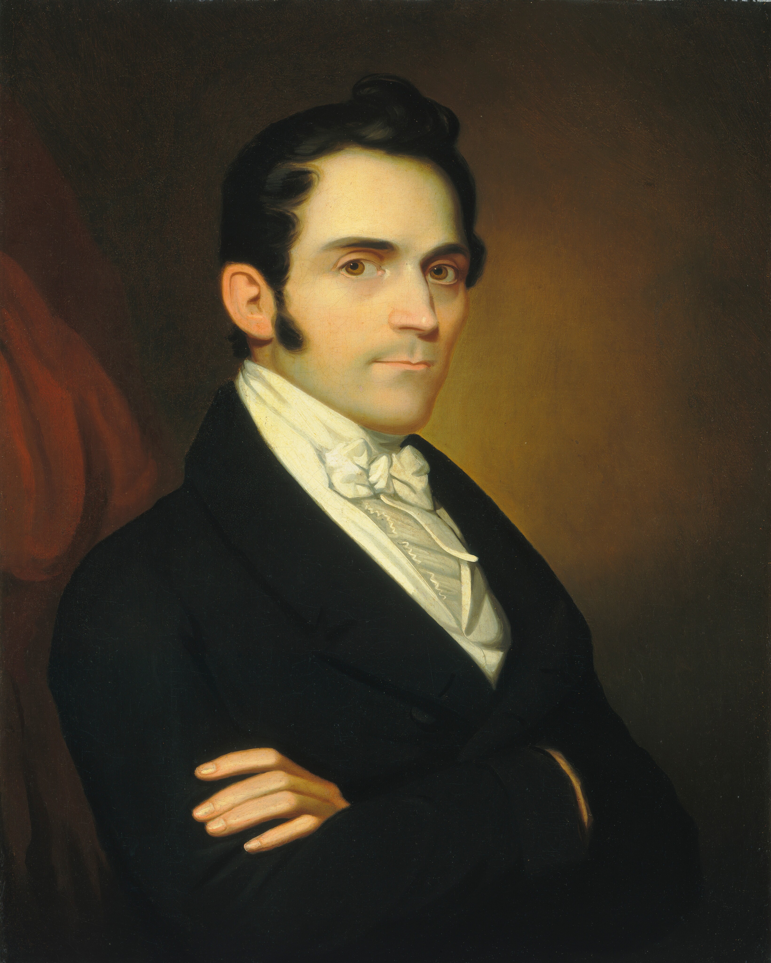 The image depicts a man's upper body. He is facing the left side of the frame but looking directly at the viewer. He has short, dark hair, sideburns, dark eyes, and a clean-shaven face. The man is wearing a black coat over a white shirt with a white cravat. His arms are crossed in front of him. The background has a gradient from dark to light brown, with a hint of red drapery on the left.