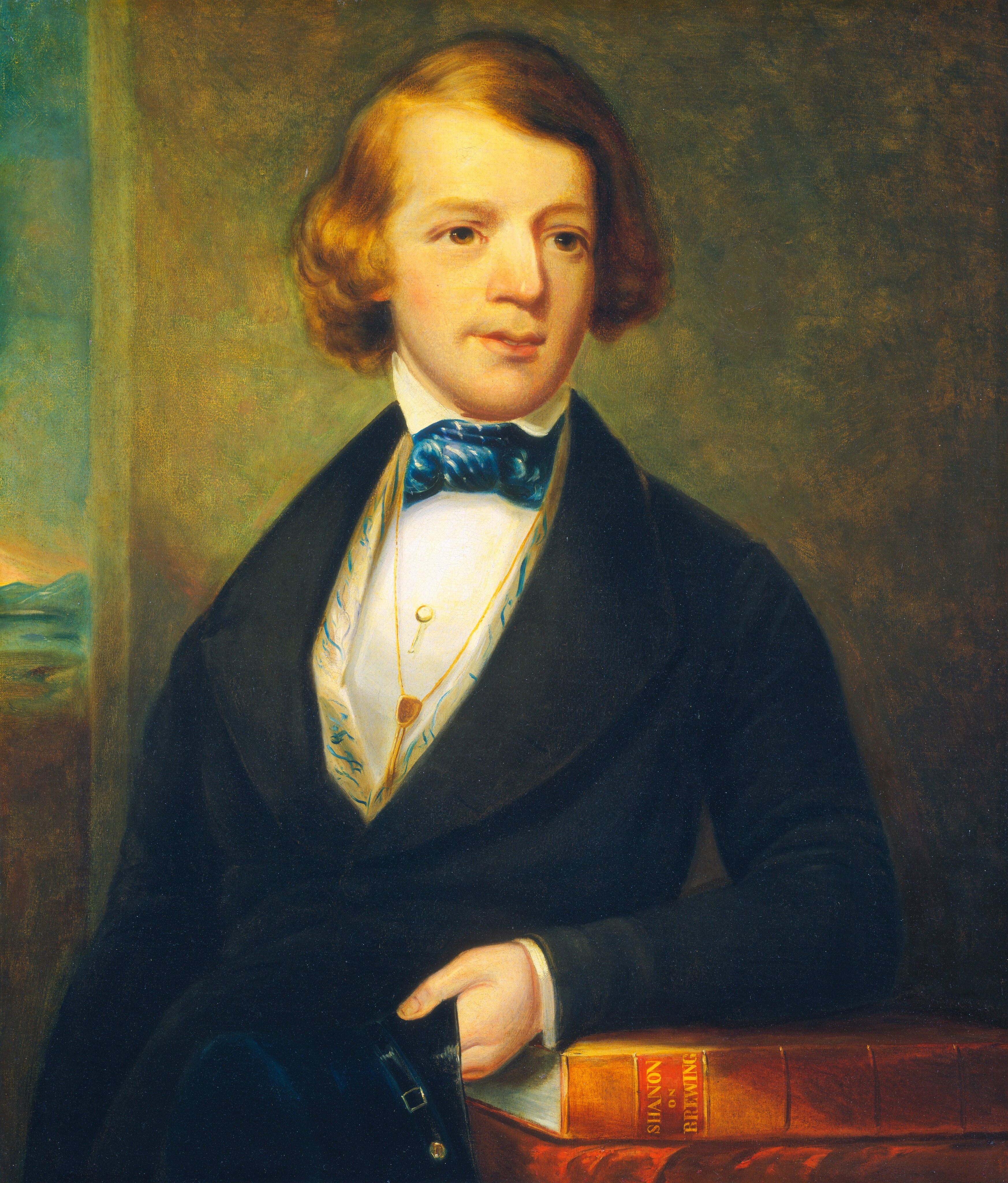 The portrait shows a young man seated with his body turned slightly to the side, facing toward the viewer. He has fair skin and neatly styled, light brown hair that is parted to one side. His face is smooth and youthful, with prominent cheekbones and a defined jawline. He wears a dark coat over a white shirt with a decorative patterned edge. A vivid blue bow tie is neatly tied around his neck. Draped over his waistcoat, a gold chain features a circular pendant and a key-like ornament. His right hand is resting on two large books positioned in front of him, one of which has 'SILVAN' and 'SHONBERG' inscribed on its spine in gold letters. The background consists of a plain, softly shaded wall, with a small portion showing a distant landscape outside a window on the left, depicting a serene natural scene.