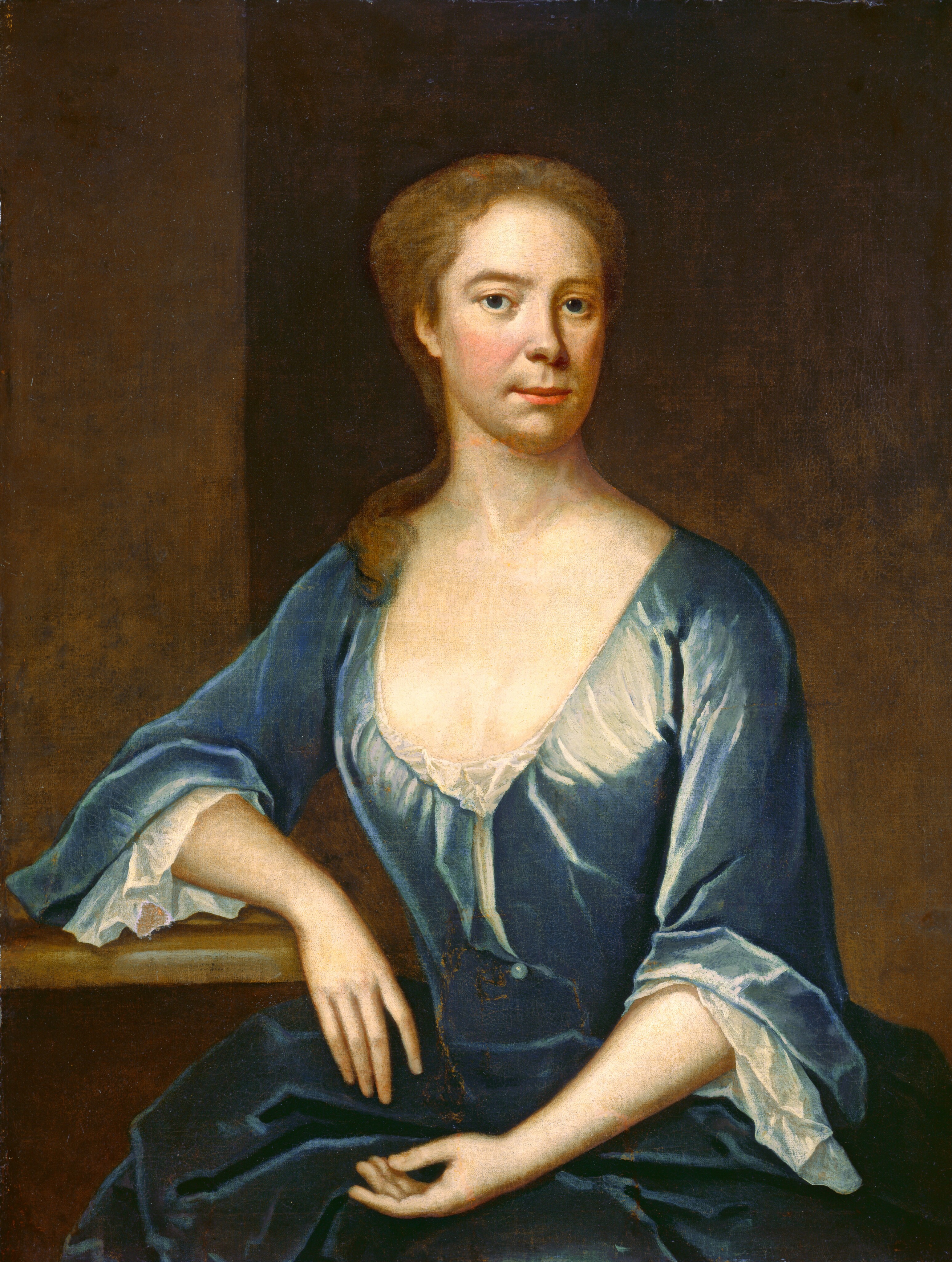 The image shows a woman seated, angled slightly to the left, with her right arm resting on a surface and her left hand on her lap. She has a composed expression with light-colored eyes and fair skin. Her hair is light brown, styled smoothly. She wears a deep blue gown with billowing sleeves trimmed with white lace. The neckline is slightly open, revealing a white chemise. The background is dark, contrasting with the subject. The woman appears dignified, without any visible jewelry.