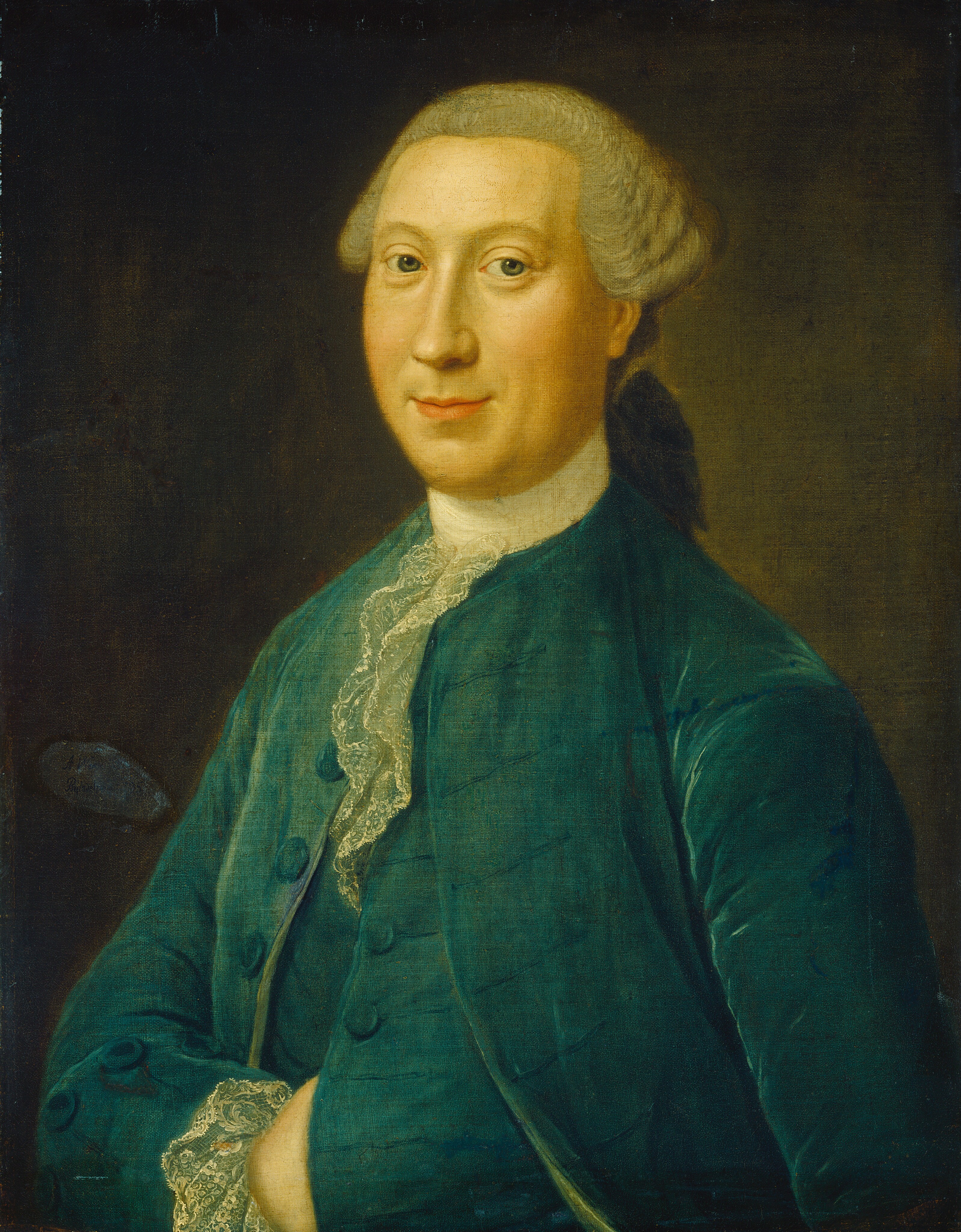The image depicts a man seated with his arms crossed, facing slightly to the side. He has fair skin, a gentle expression, and light-colored hair tied in a small ponytail. He is wearing a dark green coat over a white ruffled shirt with a plain, dark background.