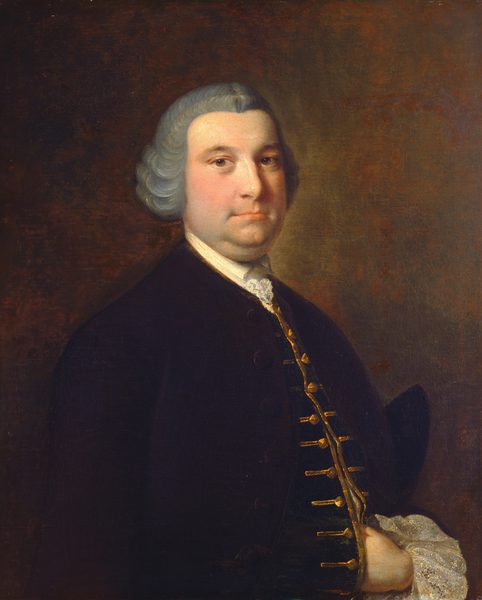 The image shows a portrait of a man with a soft, round face, a slightly double chin, small eyes, and a neutral expression. He has gray, voluminous hair styled in the fashion of the 18th century. He is wearing a dark coat with gold buttons and a white ruffled shirt underneath. One hand is hidden under his coat. The background is dark and earthy, centering focus on the subject.