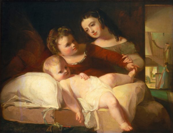 The image displays three children in a domestic setting. One boy is sitting upright, leaning towards a girl who is lying down. He has curly, light-brown hair and wears a red dress with ruffles. The girl beside him has long, dark, wavy hair and wears a light-colored gown. She appears to be holding the baby's hand. The boy is holding the baby's foot and looking kindly at the baby who has light hair and a relaxed expression. The background features a warmly-lit room with a staircase and a doorway. Two people are faintly visible descending the stairs in the adjacent section.