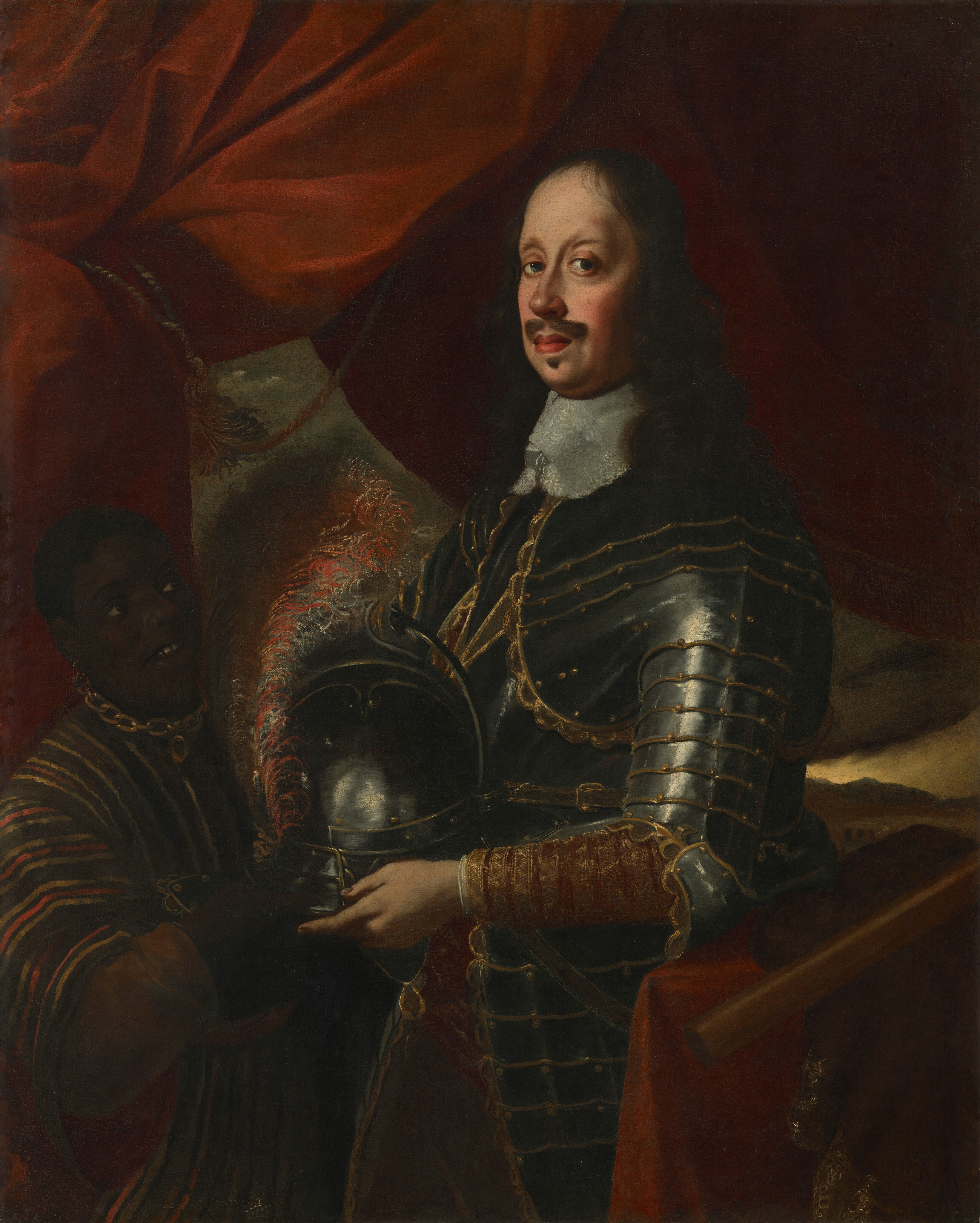 This painting shows a standing man with light skin, long curly dark hair, a mustache, and goatee. He is wearing ornate silver armor and a white ruffled collar. The overlapping plates of the armor are accented in gold at the edges. His body is turned to the left, but he faces us. His left hand holds a decorated silver helmet with red plumes. To the left is another person, partially shown in shadow, who appears to be kneeling. This person has dark skin and short hair, wears a striped garment, and has a metallic chain around their neck. They are looking up at the armored man. The background features red drapery with a glimpse of an exterior scene on the bottom right, which reveals dark mountains and a pale-yellow sky.