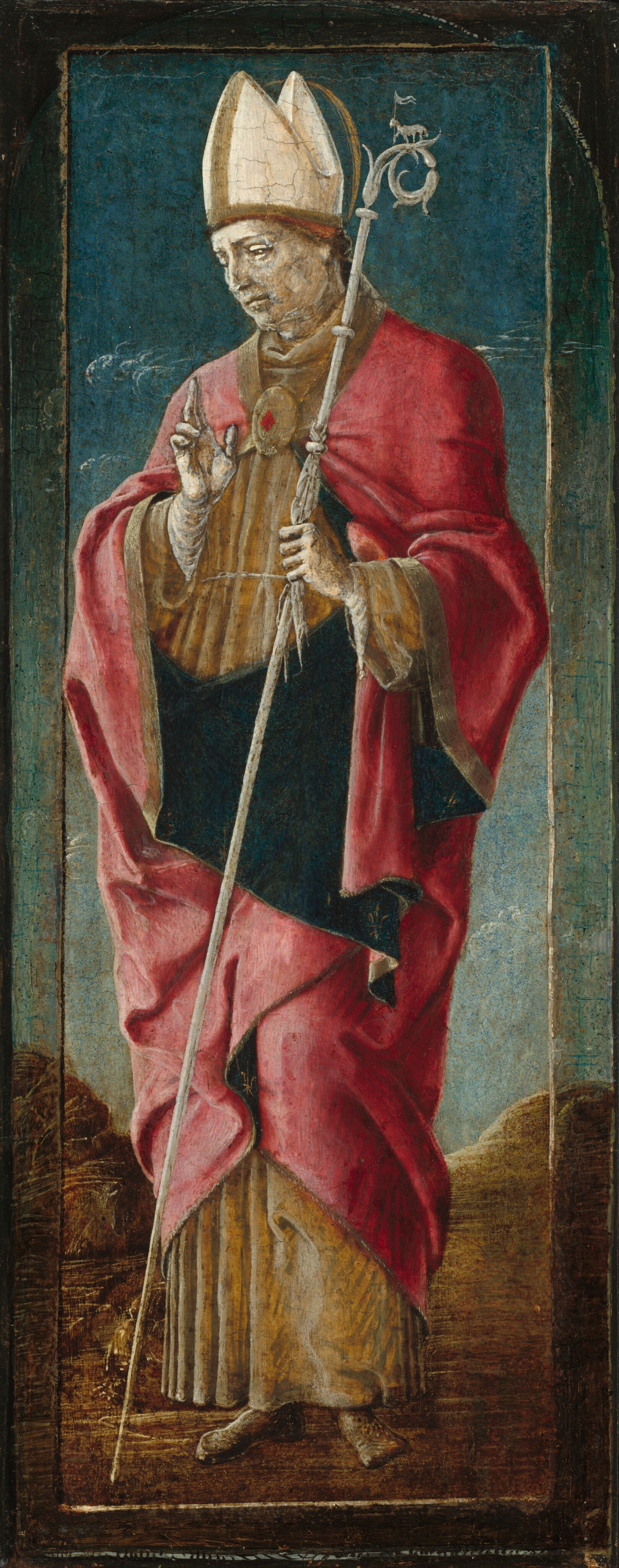 The image shows a man standing upright, holding a staff in his left hand and making a gesture with his right hand. He has prominent facial features, including a large nose and brow, along with a somber expression. His head is covered with a tall pointed mitre, and he is dressed in ecclesiastical clothing—a red robe with gold and brown accents. He wears a golden medallion around his neck. The staff he holds has intricate detailing near the top, resembling a small animal figure. The background is textured with blue and earthy tones, suggesting a landscape with hints of clouds or fog, and a brown ground.