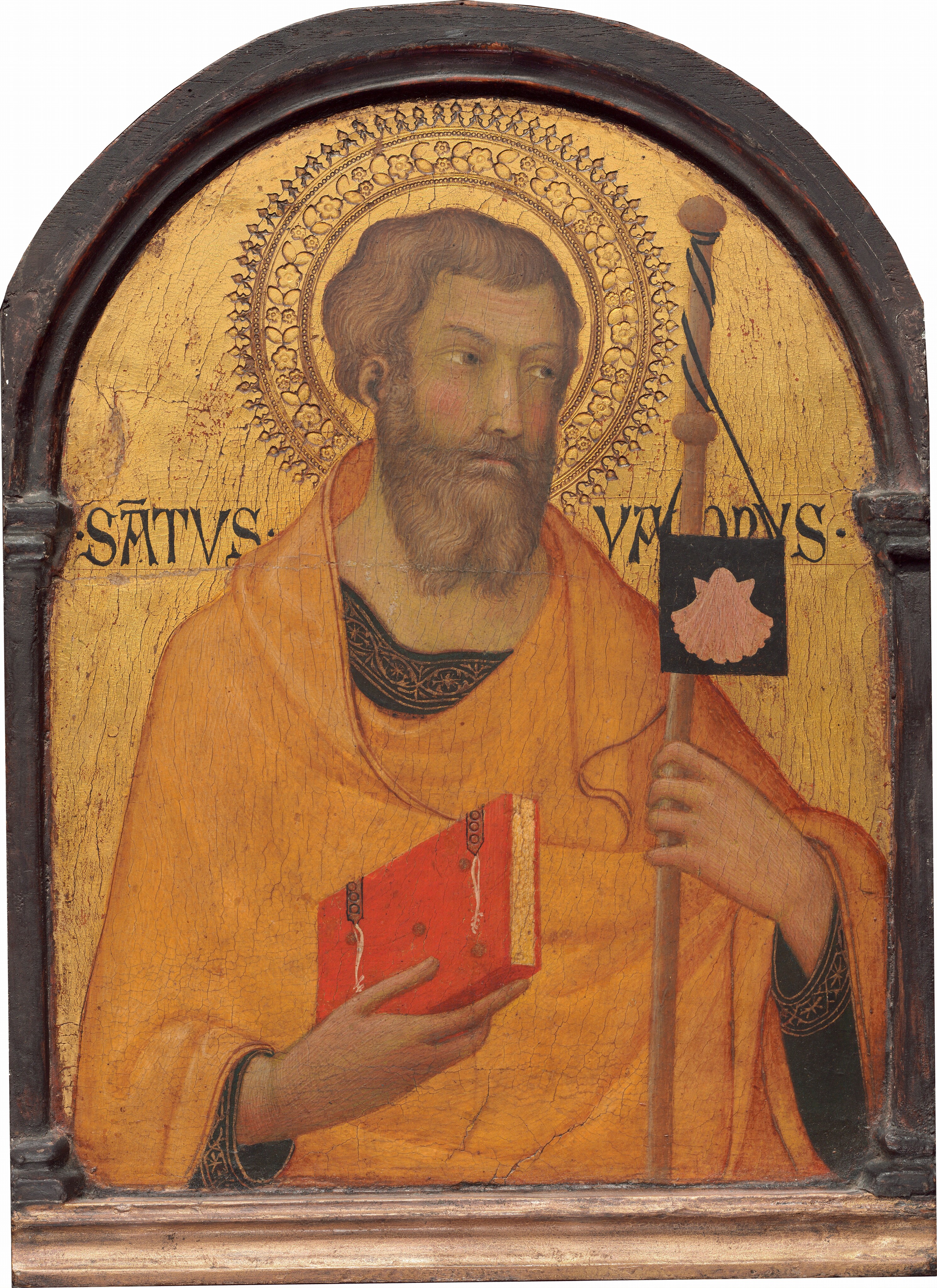 Shown from the waist up, a pale-skinned, bearded man faces us against a shiny gold background on this arched, vertical panel. The wooden panel is rounded at the top and has a wooden frame, which is painted gold along the bottom. The man’s skin has a greenish cast, but his cheeks and forehead are rosy. He has wavy, honey-brown hair and a long, forked beard. With his head tilted slightly to our right, the man looks up and off in that direction with gray eyes. He has a narrow, straight nose, a thin pink mouth, and small ears. He holds a red book in front of his chest with his right hand, to our left. The book has brown hinges, and the edges of the pages are gold. In his other hand, he grasps a wooden staff tied at the top with a small, black, square flag displaying a petal-pink scallop shell. His harvest-yellow cloak drapes over his shoulders, across his body, and over his left arm. Under the cloak, he wears a black tunic with wide gold trim patterned with starburst-like forms within pointed ovals along the neckline and sleeves. A double ringed halo punched with a flower pattern surrounds the man’s head against the glimmering gold background. There is a noticeable network of cracks across the painting's surface, especially on the gold background behind the man. Inscriptions next to his shoulders read “SATVS” on our left and “YACOBVS” on our right.